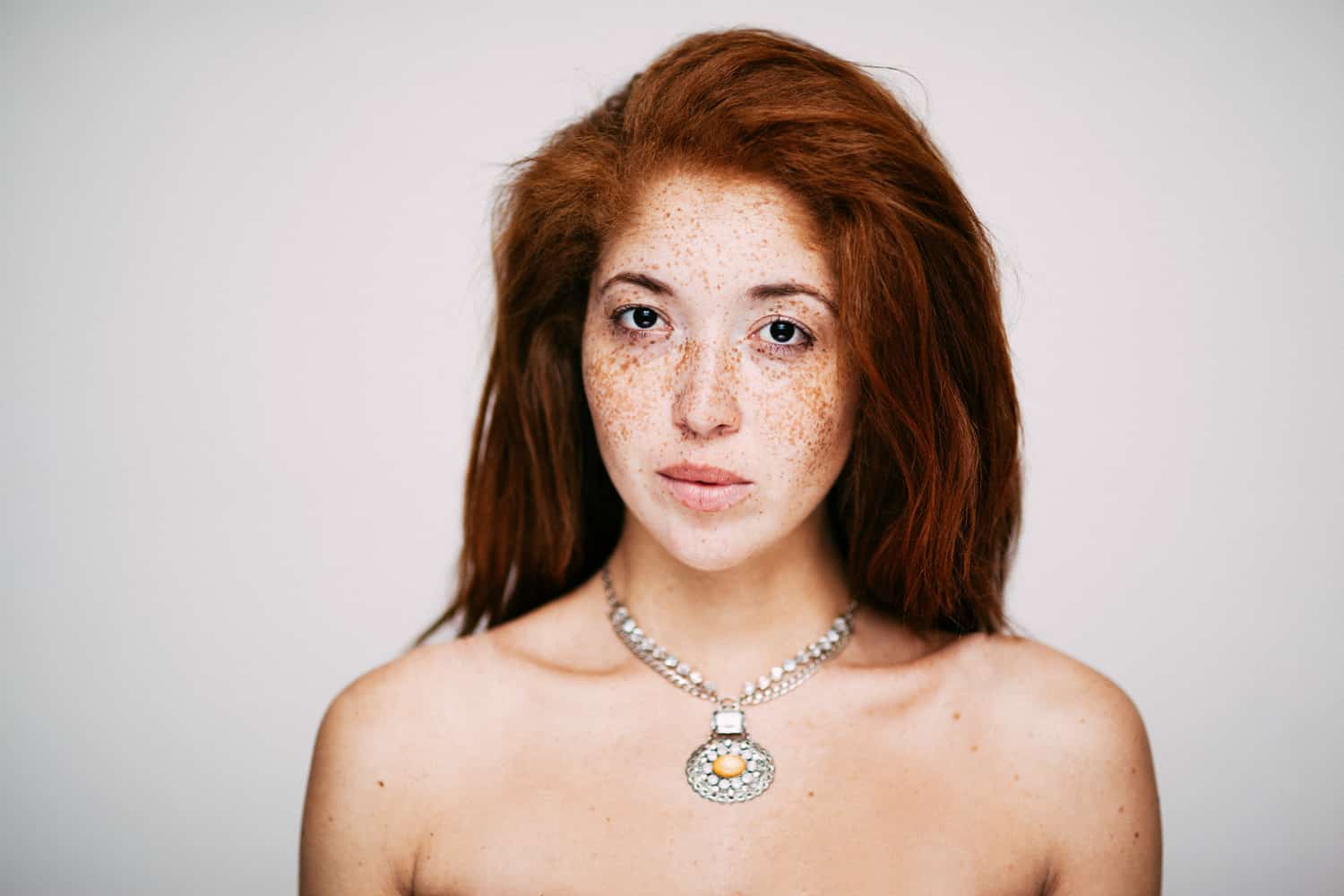 A professional portrait photographer capturing the beauty of a woman with freckled hair and a necklace.