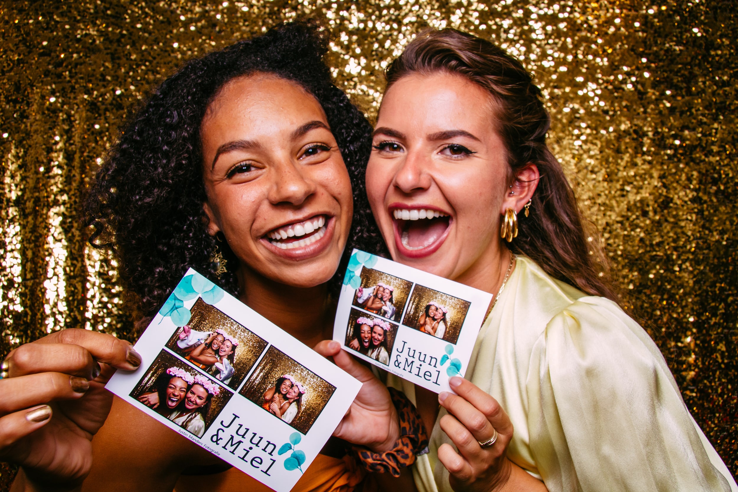 Two women in a photobooth at a wedding while holding up photos.