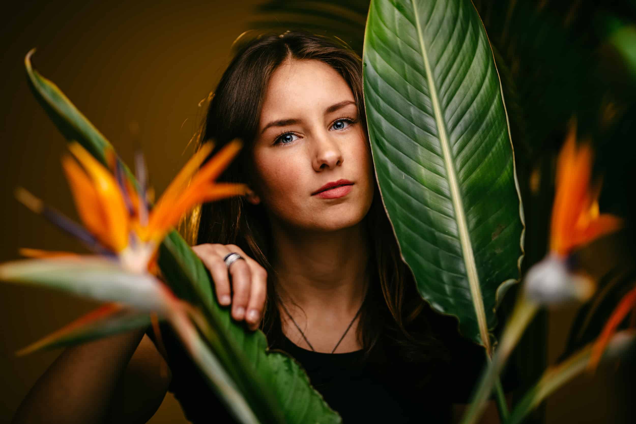 A professional portrait photographer captures a woman's pose in front of a bird of paradise plant.