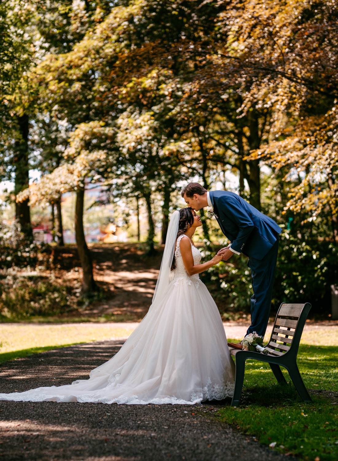 Een bruid en bruidegom die elkaar hartstochtelijk kussen op een bankje in het park en het mooie moment vastleggen door de lens van een ervaren bruiloftsfotograaf.