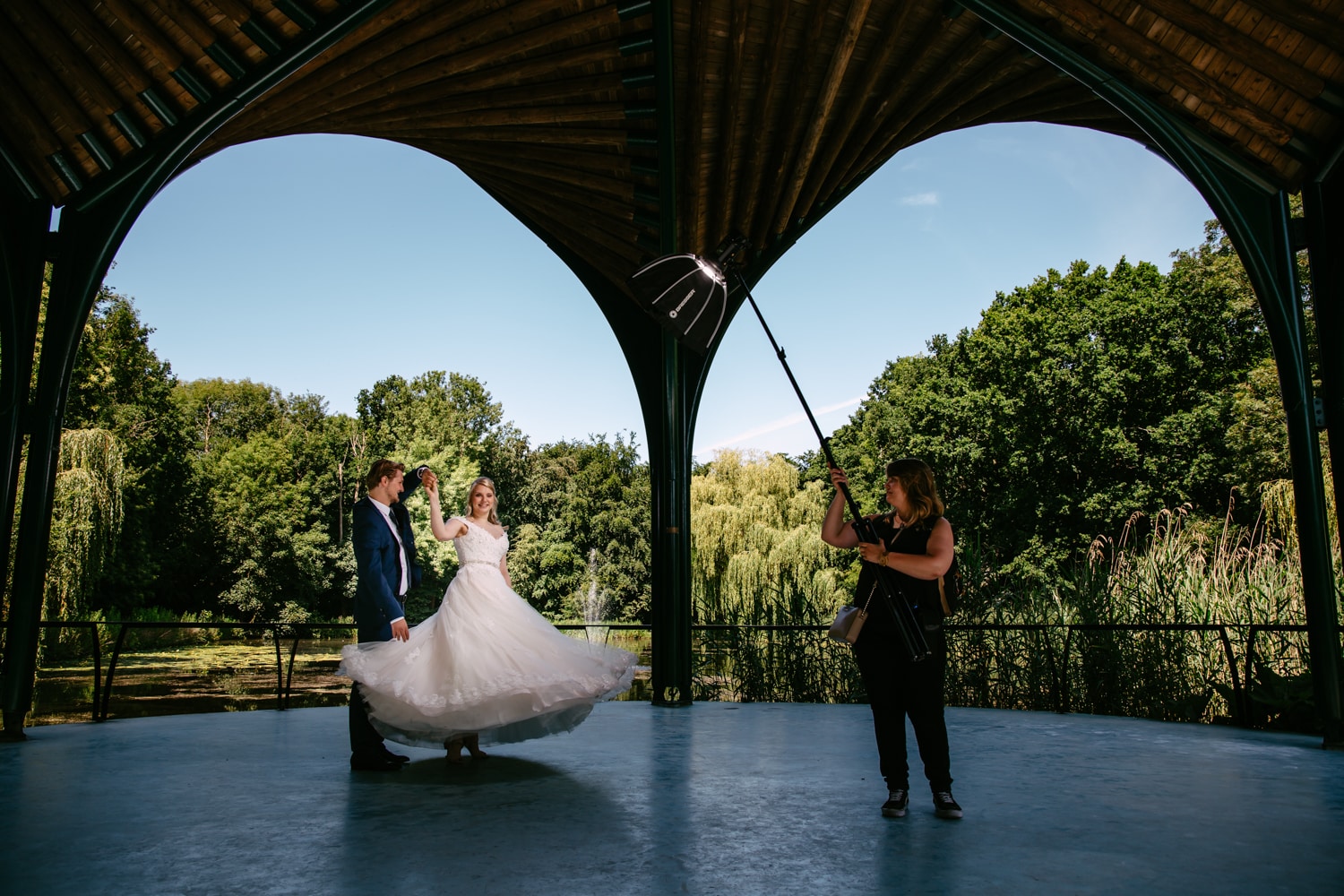 A bride and groom pose for their wedding photographer in a gazebo.