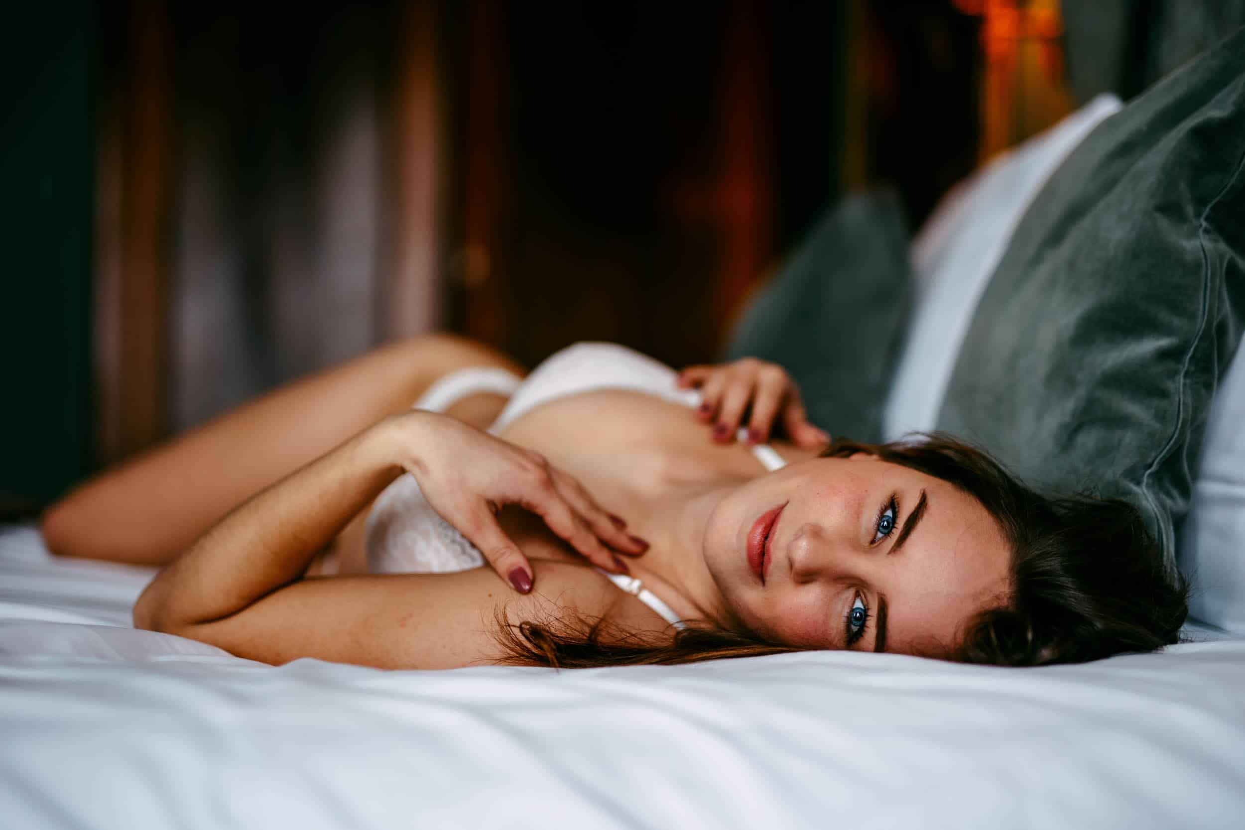 A beautiful woman, lying elegantly on a boudoir bed in enchanting lingerie.