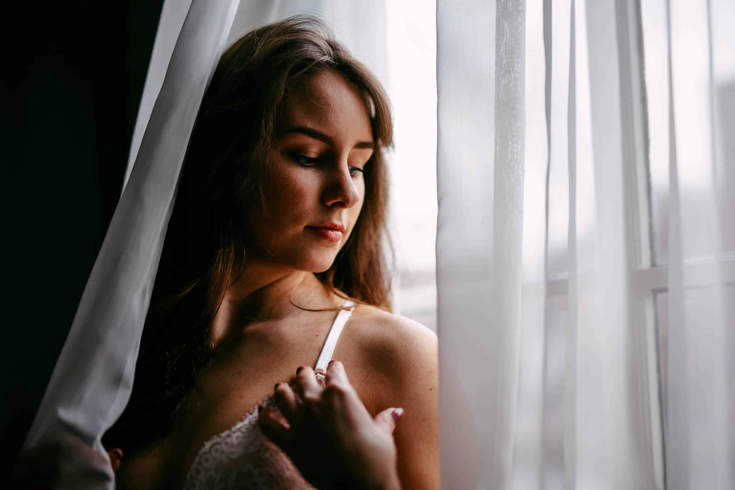 Een vrouw in een boudoir die uit een raam kijkt.