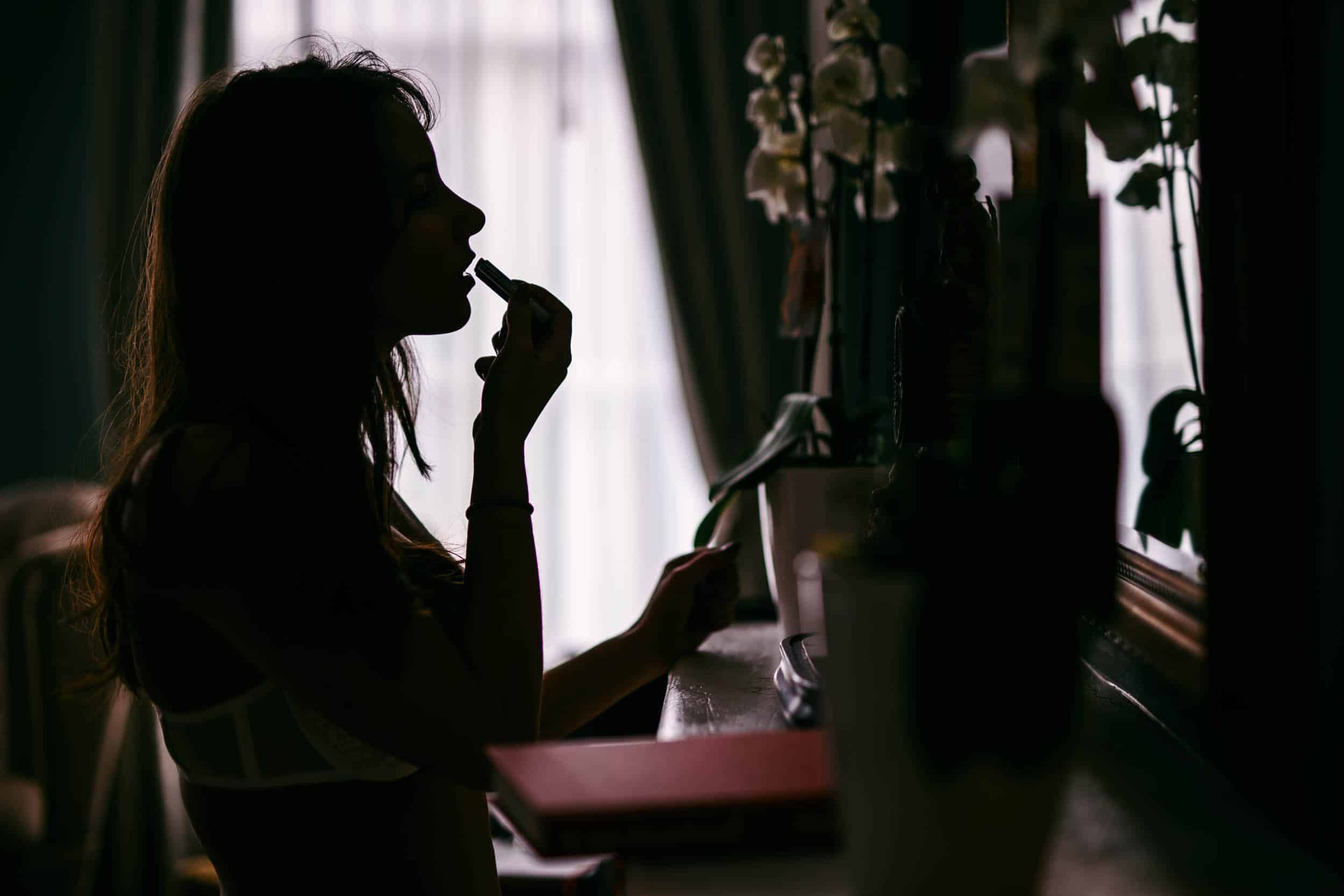 A woman brushes her teeth in front of a boudoir mirror.