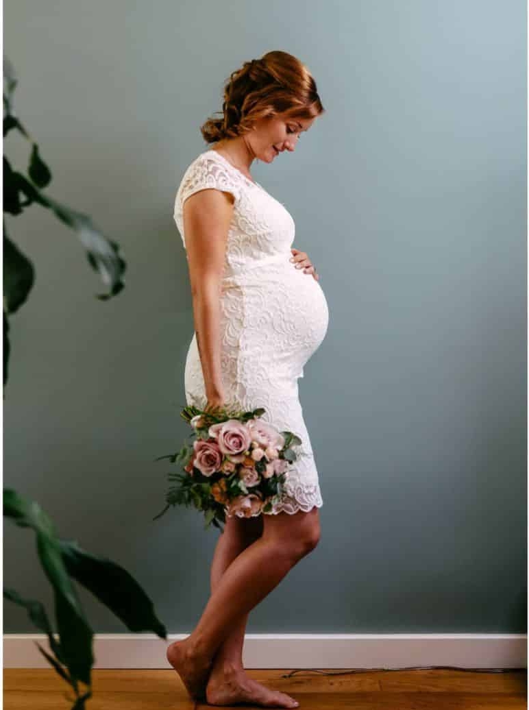 A pregnant woman in a white dress carrying a bouquet.