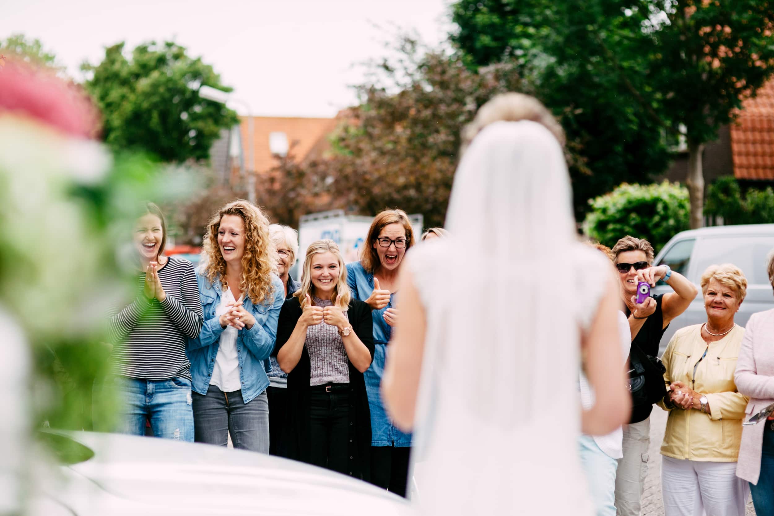 Een trouwdagbruid en haar bruidsmeisjes staan voor een auto.