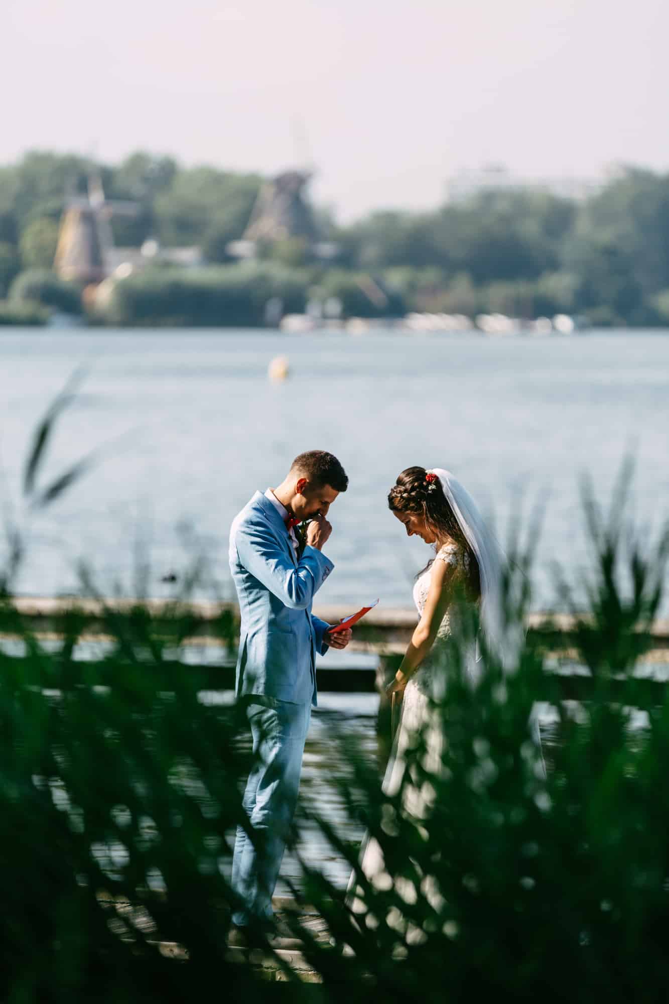Een bruid en bruidegom die trouwgeloftes uitwisselen op een kade naast een rustig water.
