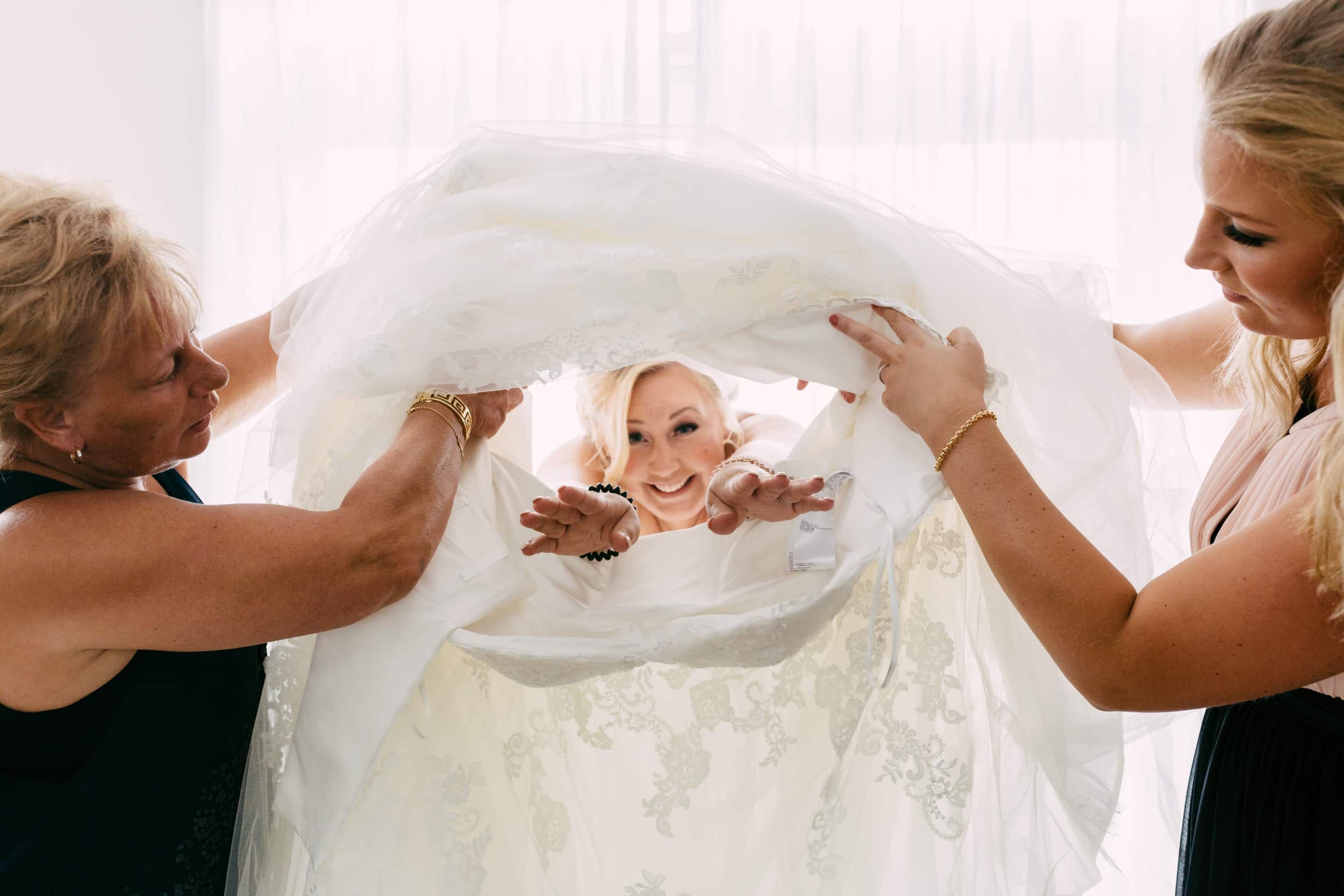 Tijdens de ondertrouw wordt een bruid door haar bruidsmeisjes aan haar trouwjurk geholpen.