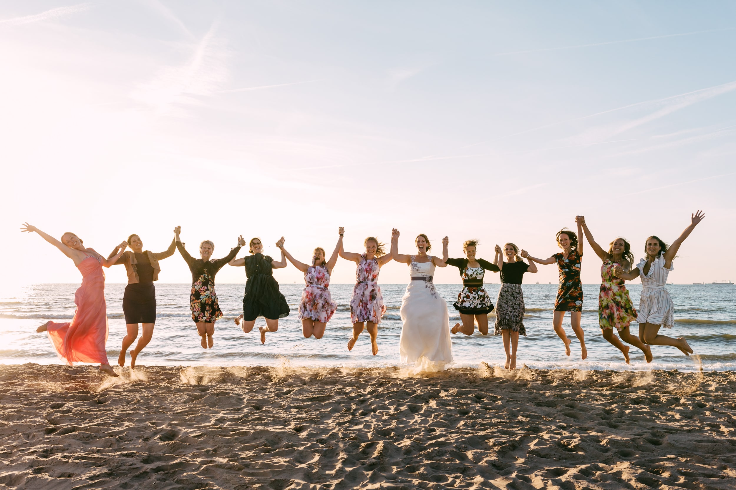 Een groep bruidsmeisjes die tijdens een bruidsdouche in de lucht springen op het strand.