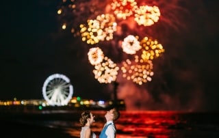 Een bruid en bruidegom staan op het strand in Den Haag met vuurwerk op de achtergrond.