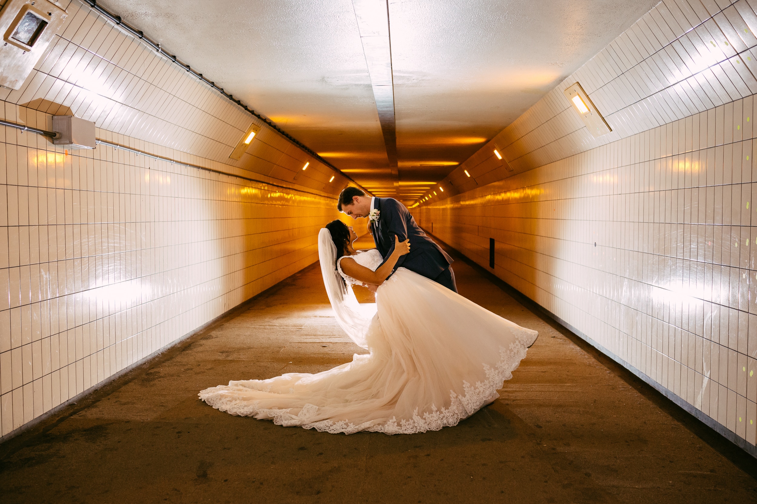 Een bruid en bruidegom kussen in een tunnel.