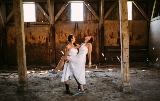 Twee vrouwen omhelzen elkaar liefdevol in een oude schuur tijdens hun Trouwfotos-sessie.