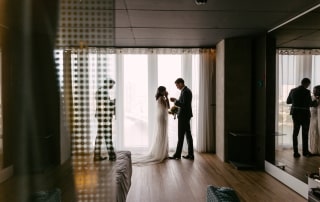Een bruid en bruidegom poseren voor trouwfoto's voor een spiegel in een hotelkamer.