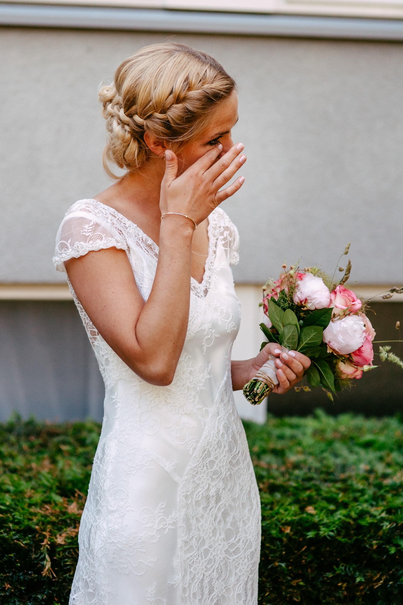 A Bohemian bride in a white wedding dress covering her face.