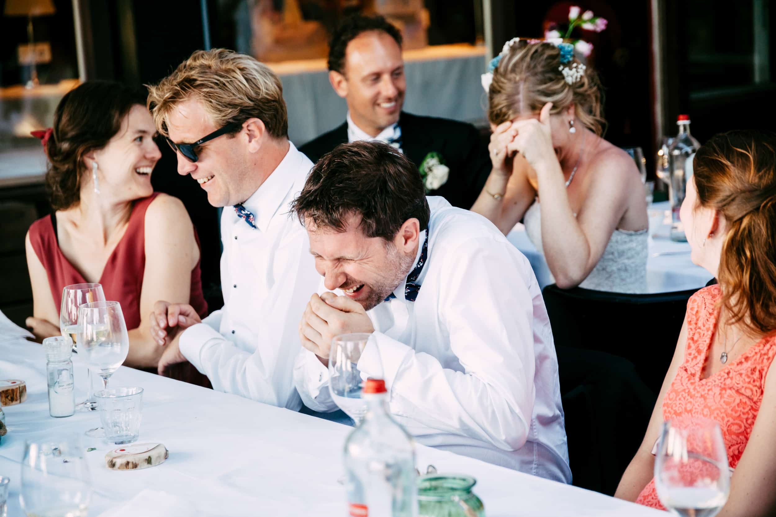 A group of people laughing and enjoying a Lacy speech at a wedding table.