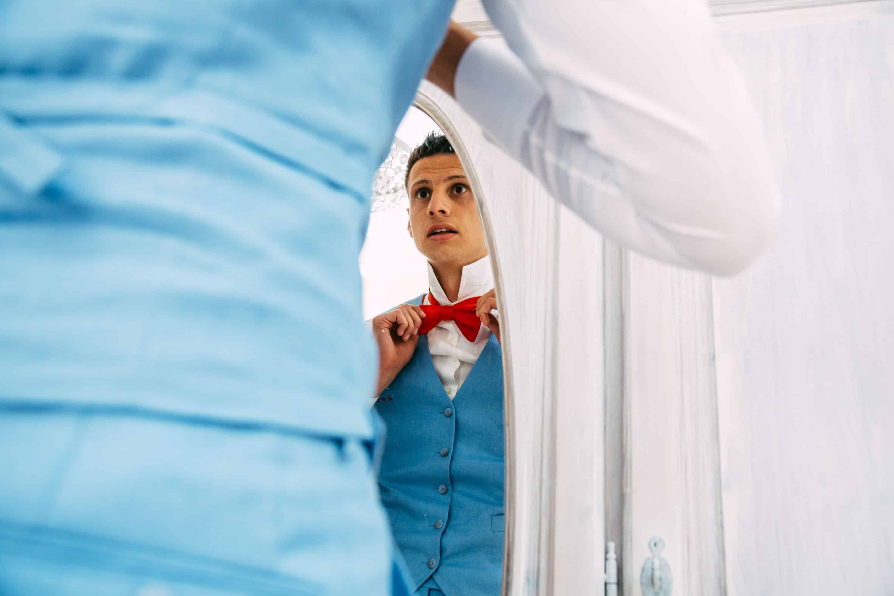 Een man past op zijn trouwdag zijn stropdas aan in een spiegel.