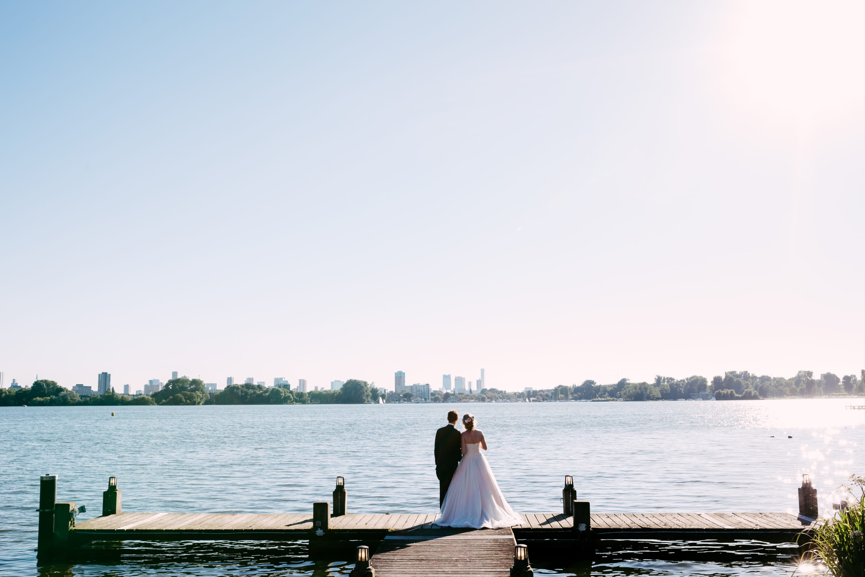 A bride and groom stand on a quay in front of a beautiful lake and embrace each other on their wedding day.