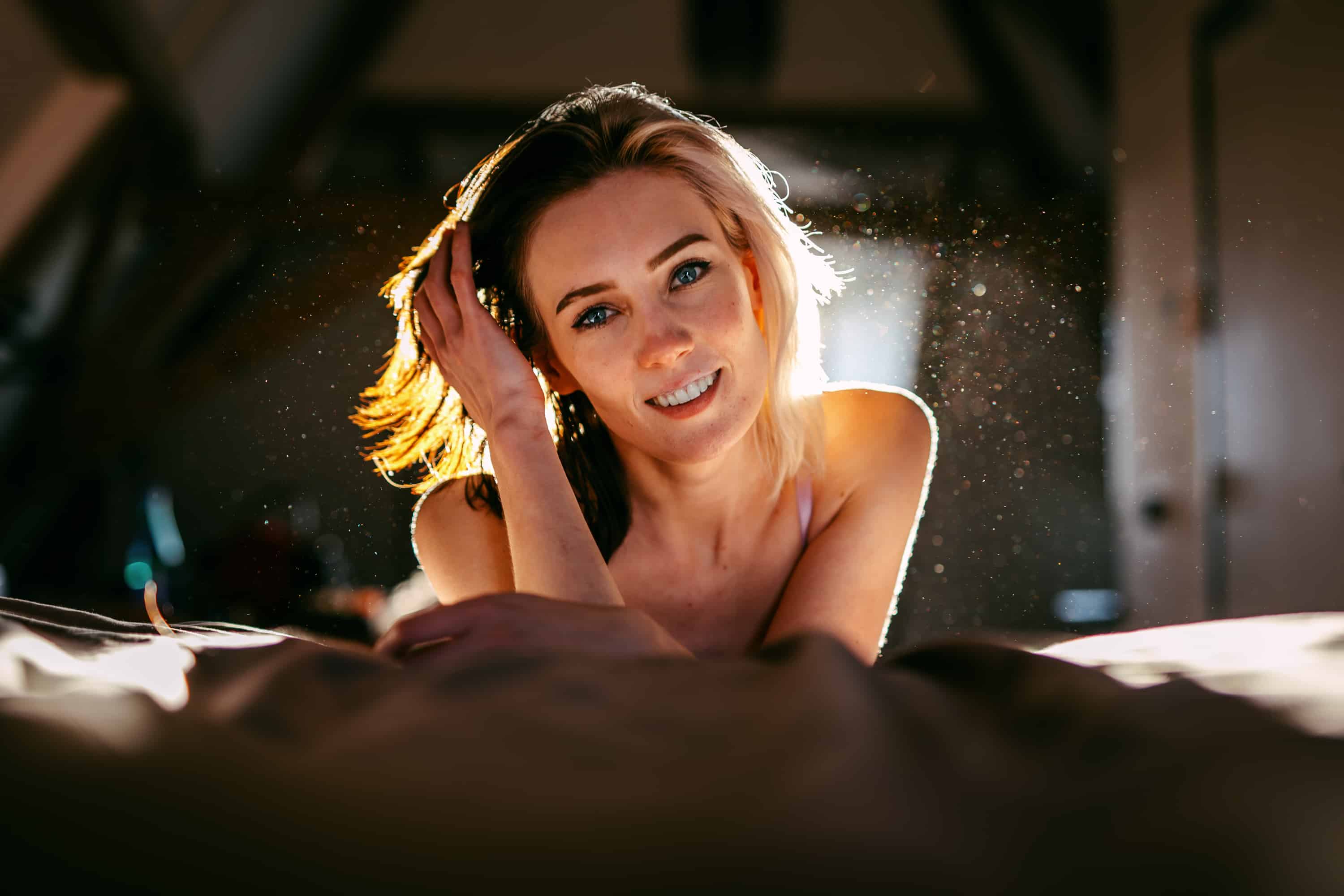 Een jonge vrouw poseert verleidelijk op een bed tijdens een boudoirshoot in een donkere kamer.