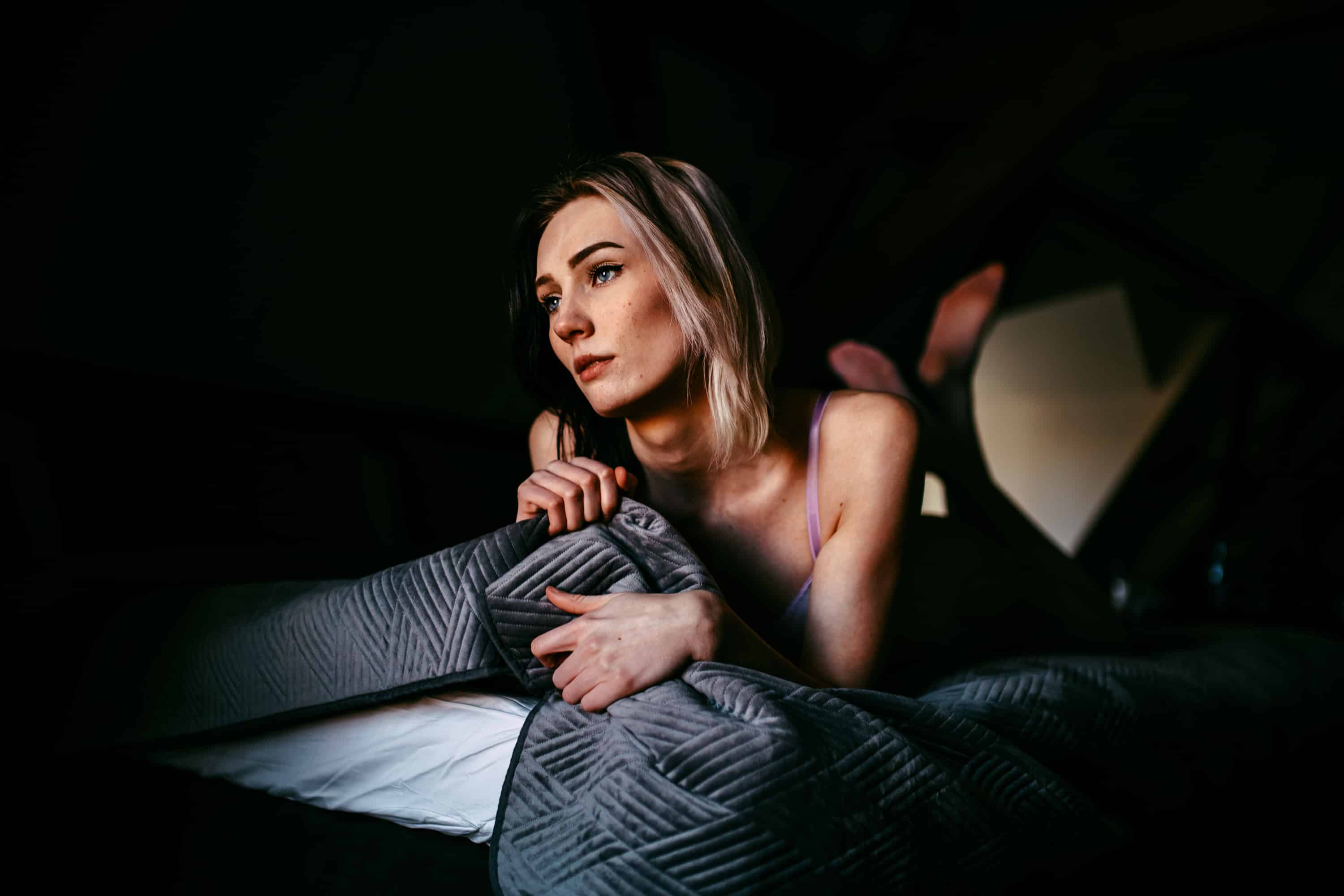 Een vrouw die een boudoirshoot doet in het donkere bed.