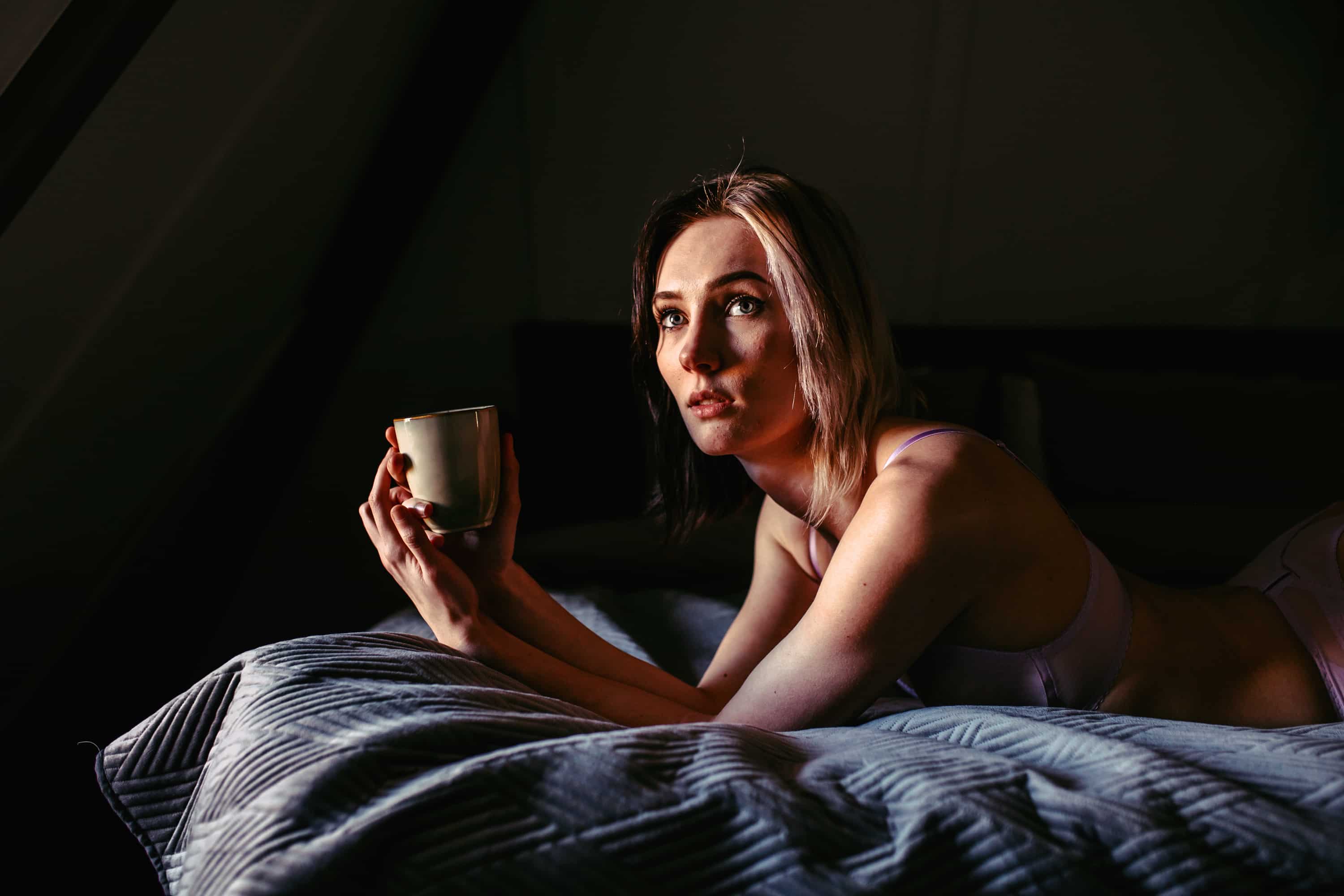 A boudoir shoot of a woman in Westland, as she relaxes on her bed and gently rocks a cup of coffee.