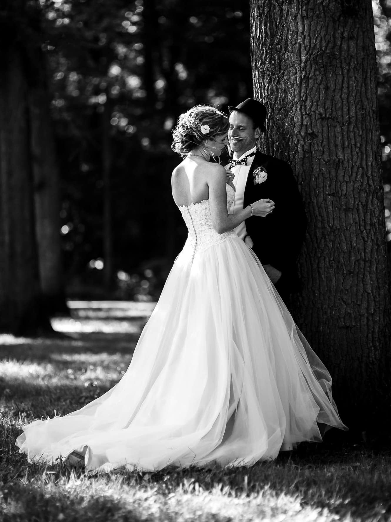 Zwart-wit trouwfotografie van een bruid en bruidegom knuffelend onder een boom.