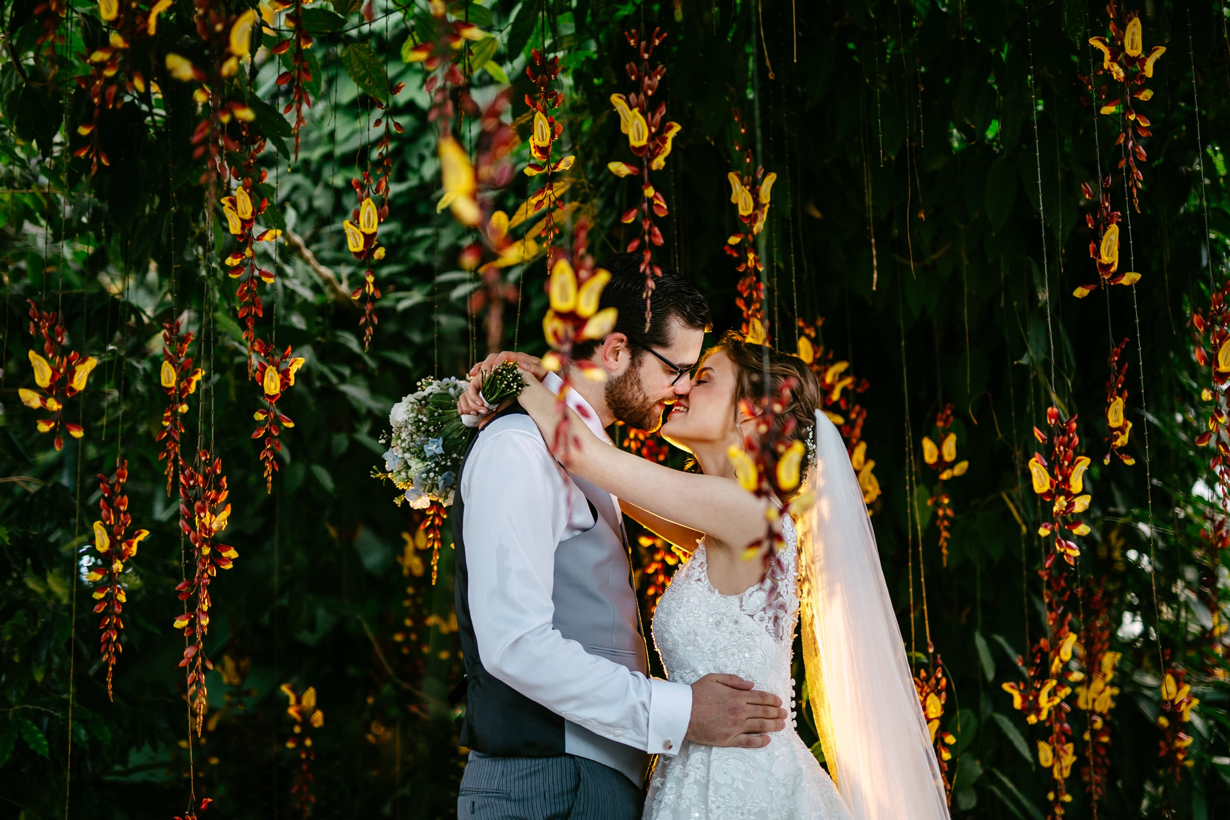 Beschrijving: Een bruid en bruidegom omhelzen elkaar voor een prachtige bloementuin tijdens hun huwelijksthemaceremonie.