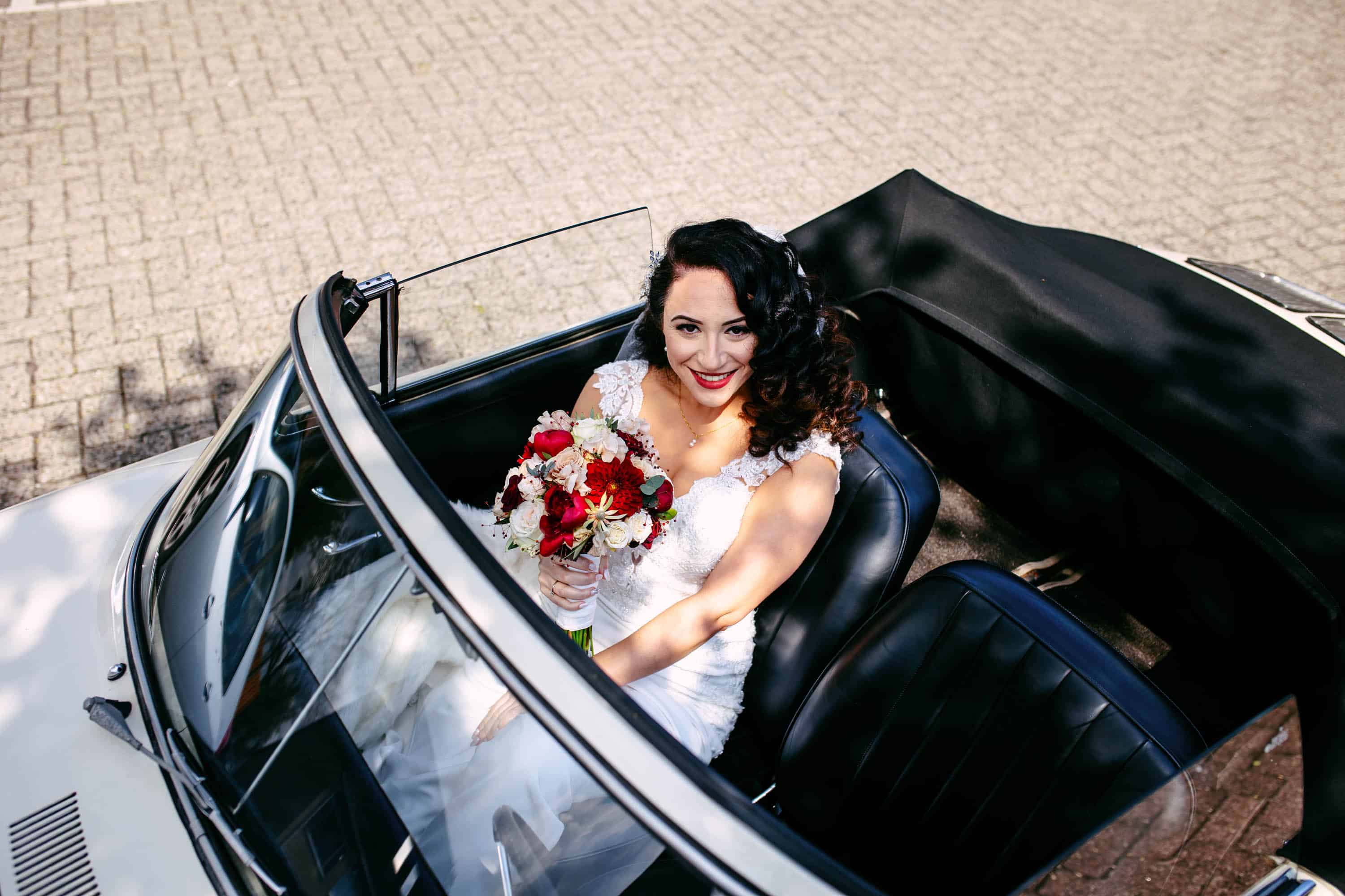 A bride sits in the back seat of a convertible.
