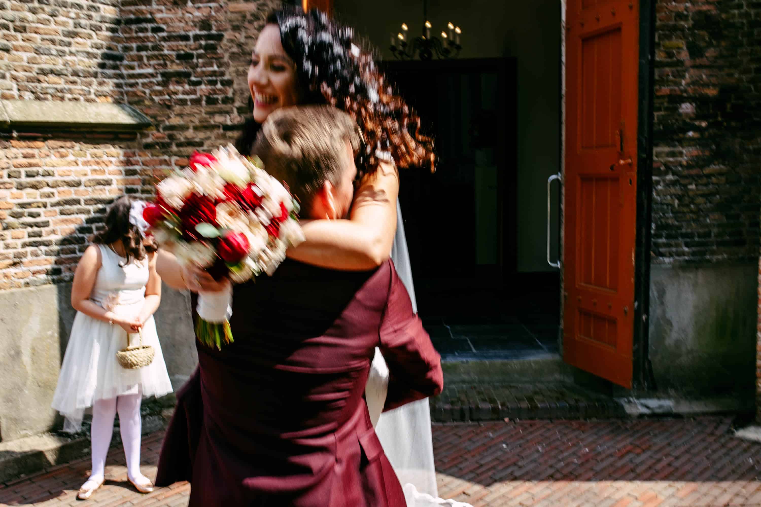 A bride and groom hug in front of a brick building.