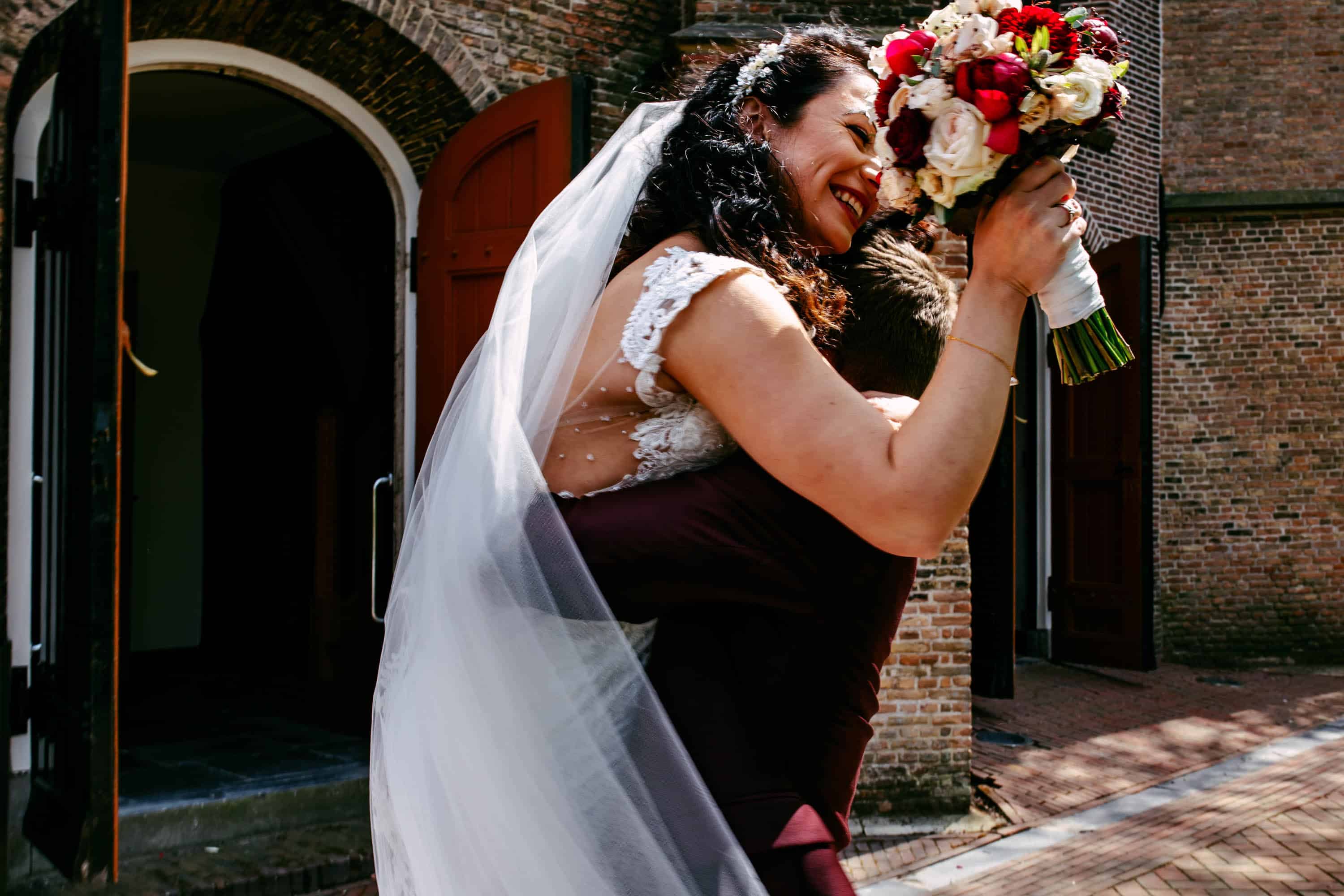 A bride and groom hug in front of a church.