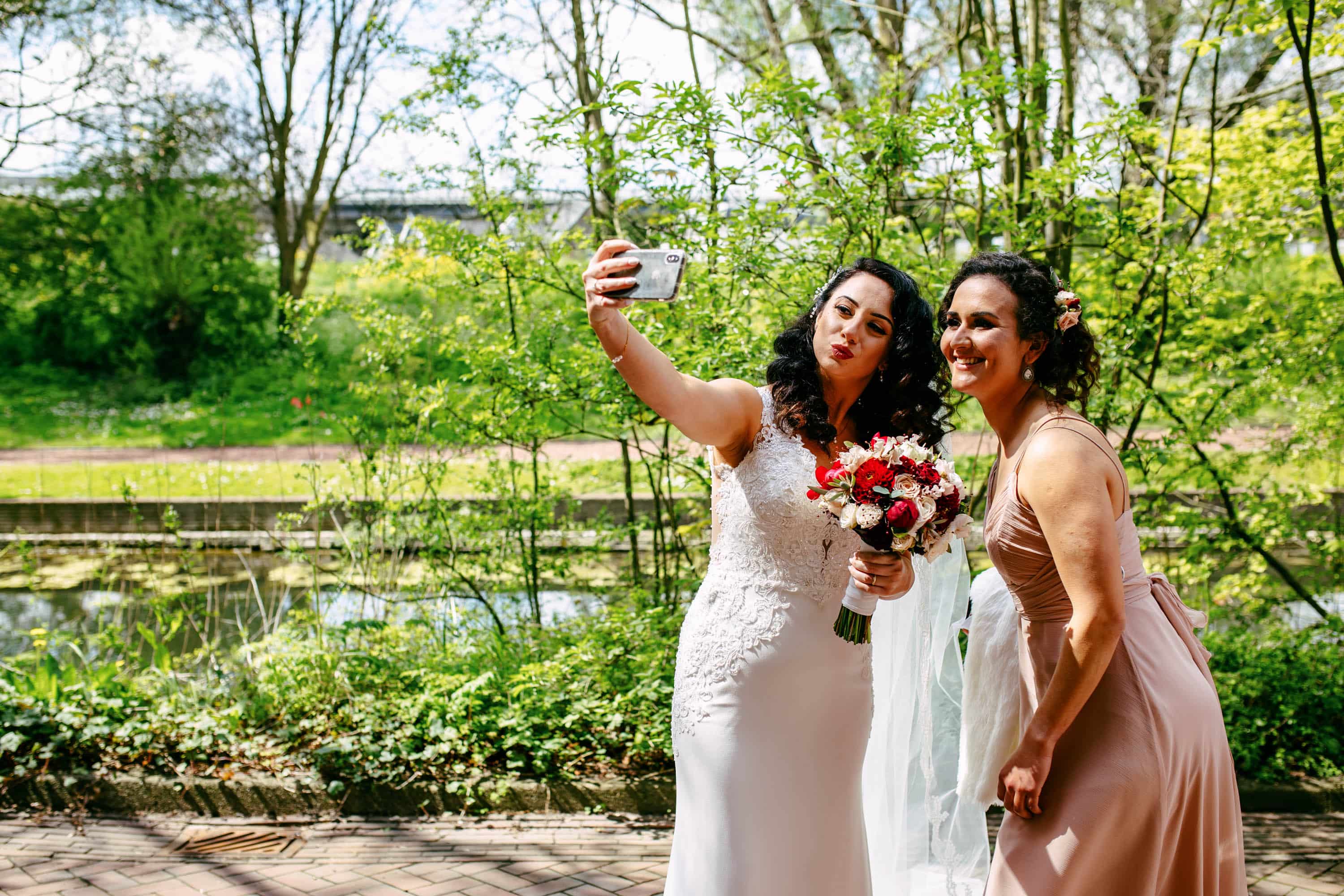 Two bridesmaids taking a selfie in a park.