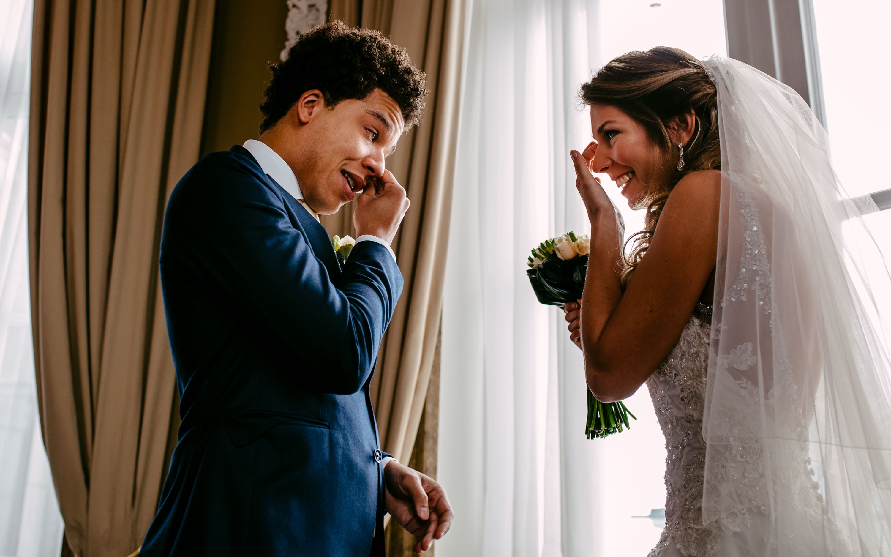 Een trouwfotografie waarbij een bruid en bruidegom een hartstochtelijke kus delen voor een raam.