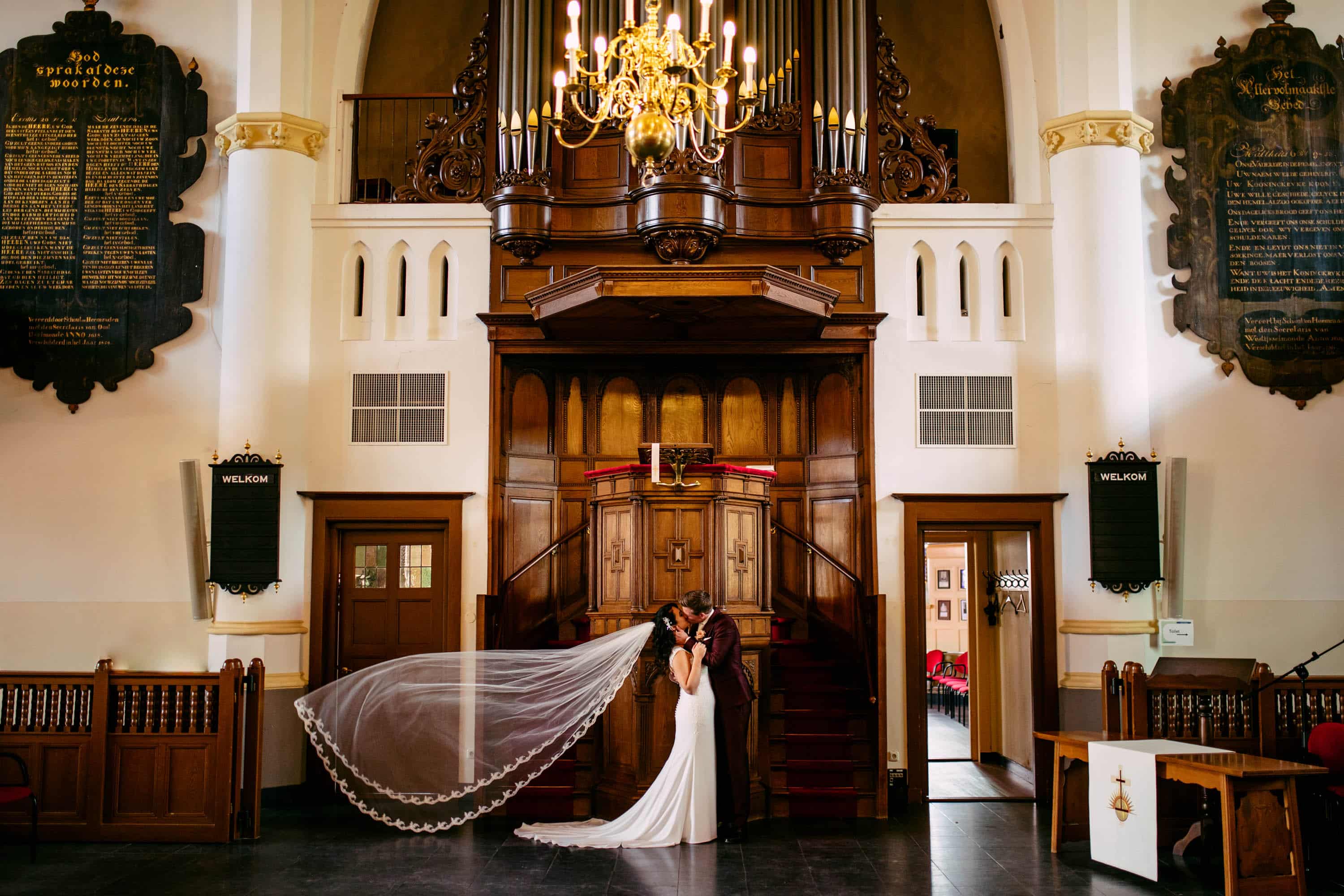 A bride standing with a veil in front of an ornate church.