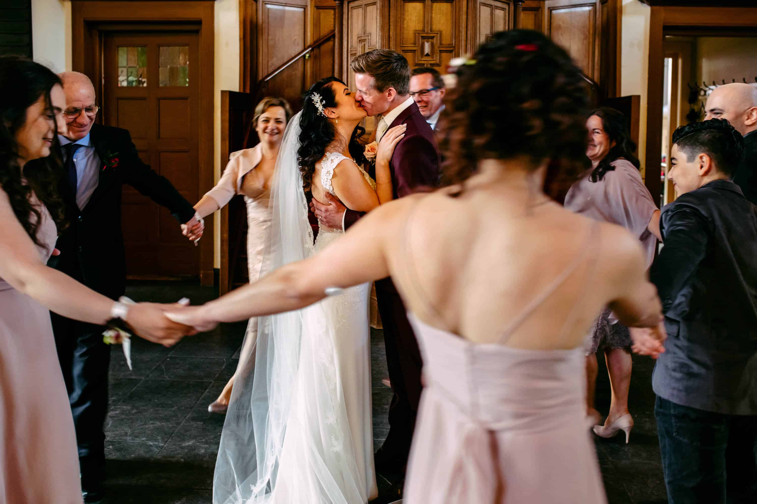 A bride and groom dance in a room with other people.