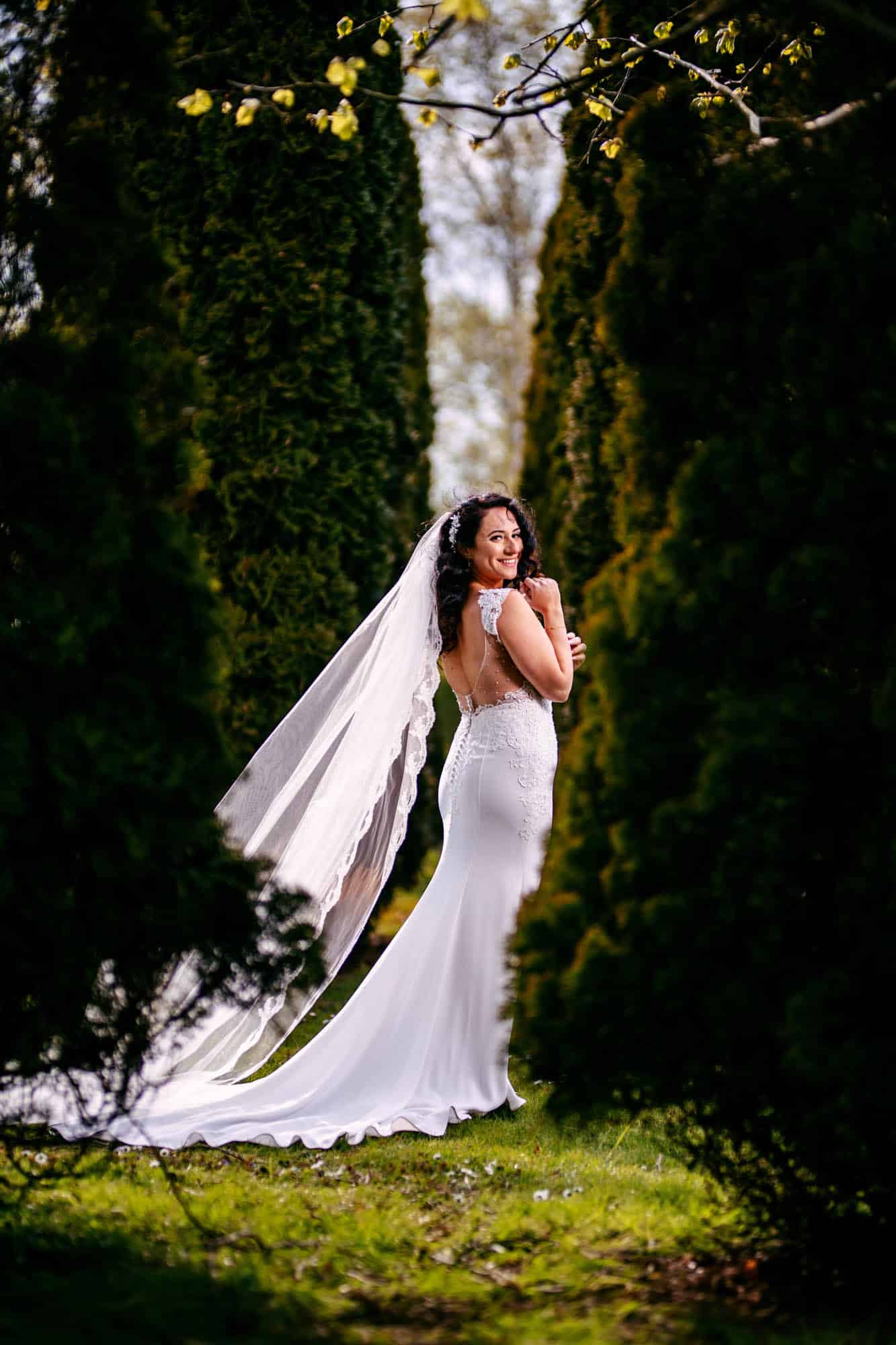 A bride in a wedding dress stands in the middle of the bushes.