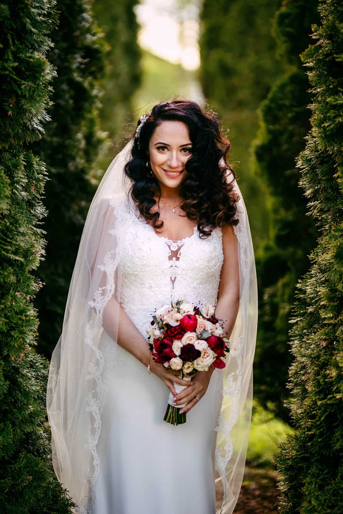 A bride in a wedding dress stands in a grove of trees.