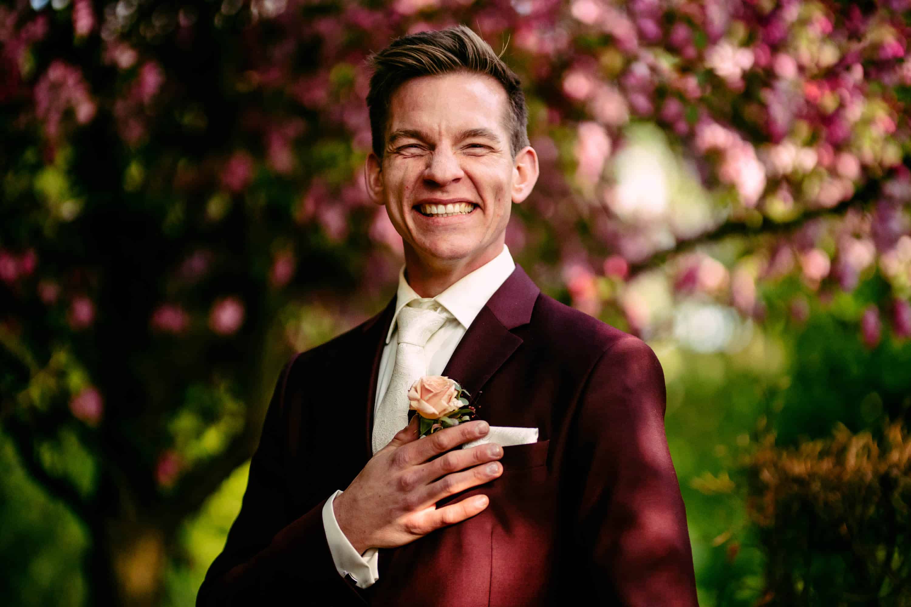 A man in a suit smiles in front of a flowering tree.