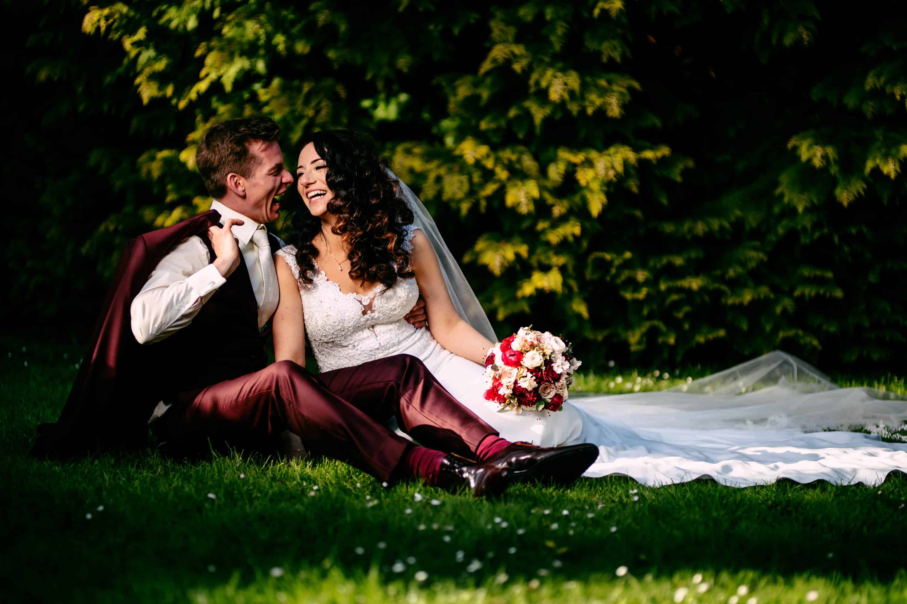A bride and groom sitting on the grass.