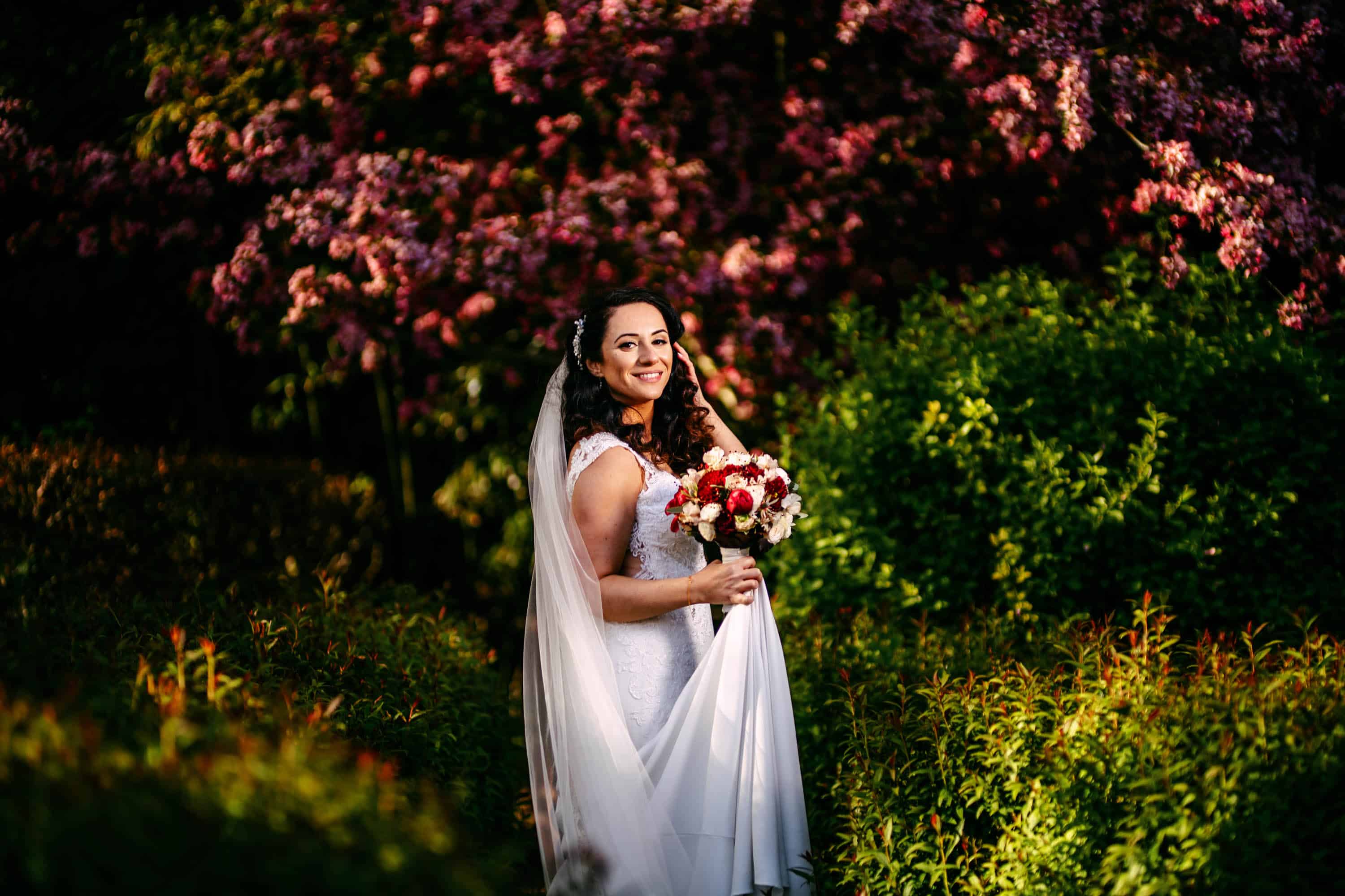 A bride in a wedding dress poses in front of a flowering tree.