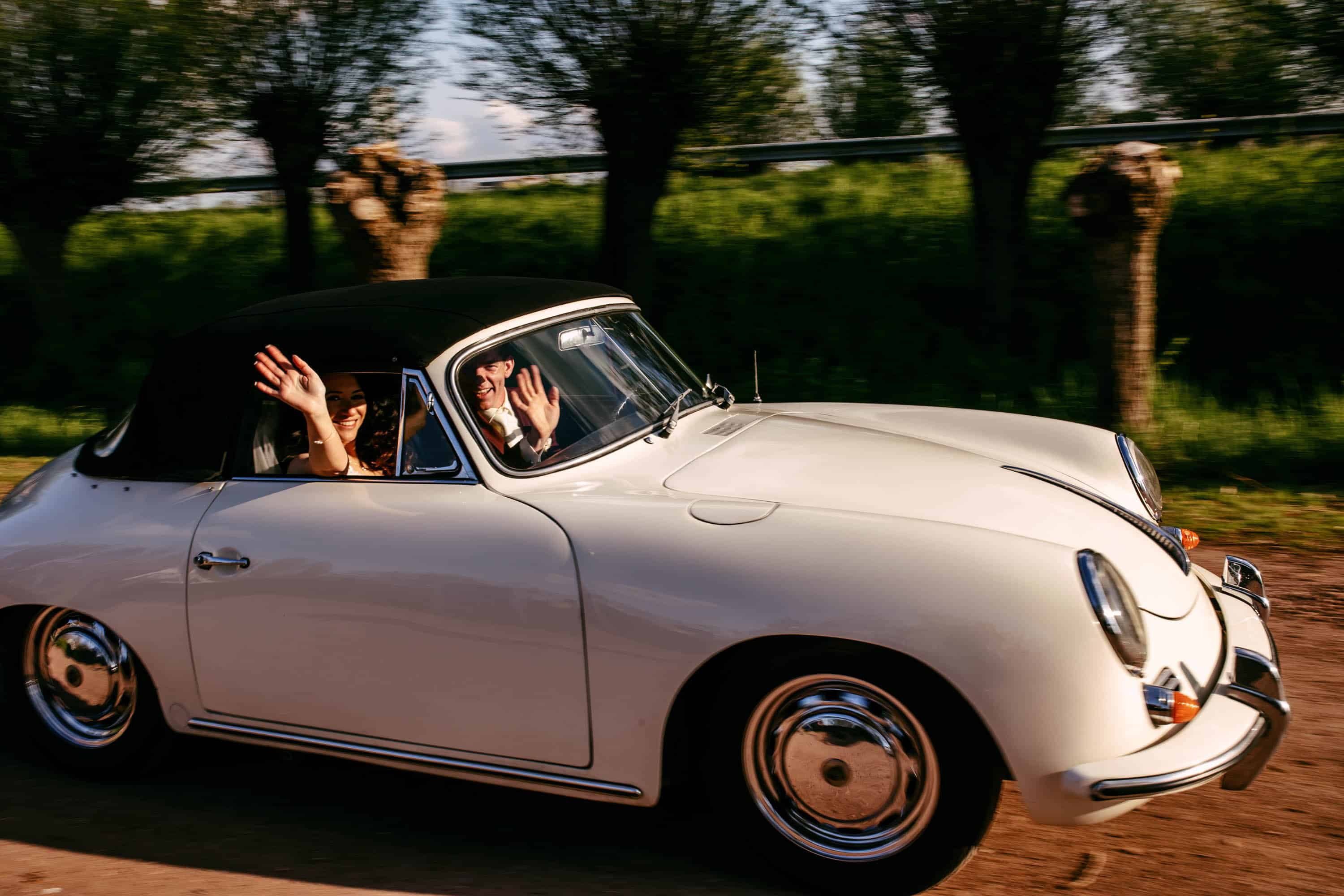 A woman drives down a country road in a white Porsche car.