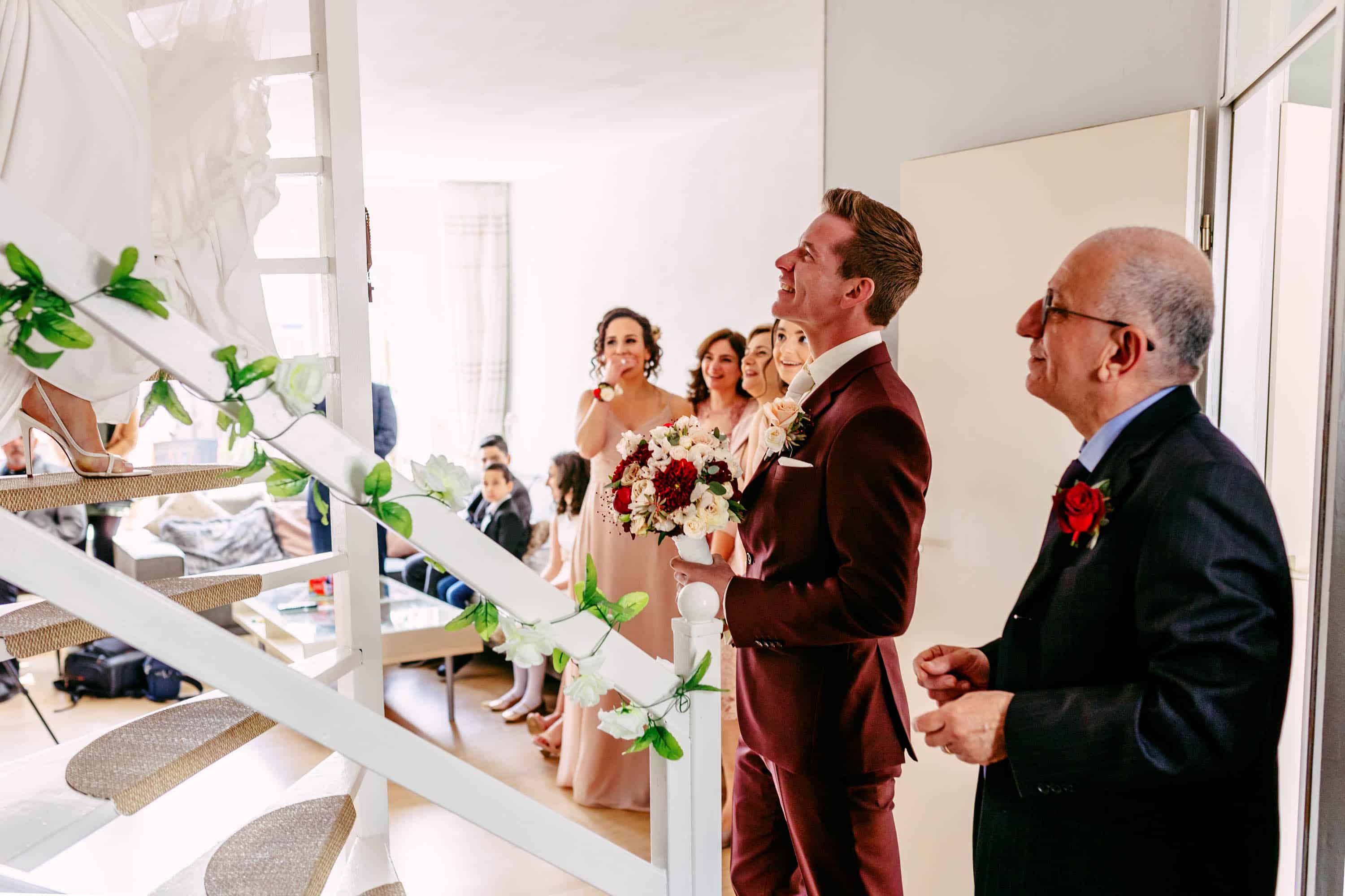 A bride and groom stand in front of a staircase.