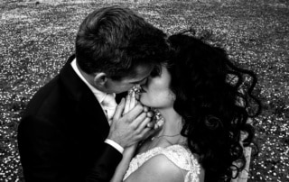         Beschrijving: Een bruid en bruidegom poseren voor trouwfoto's, liefdevol kussend in een veld met madeliefjes.