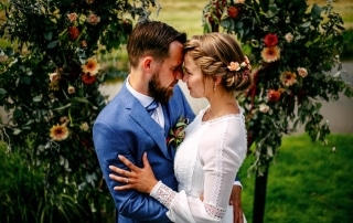 Een bruid en bruidegom omhelzen elkaar voor een bloemenboog, waardoor prachtige trouwfoto's ontstaan.