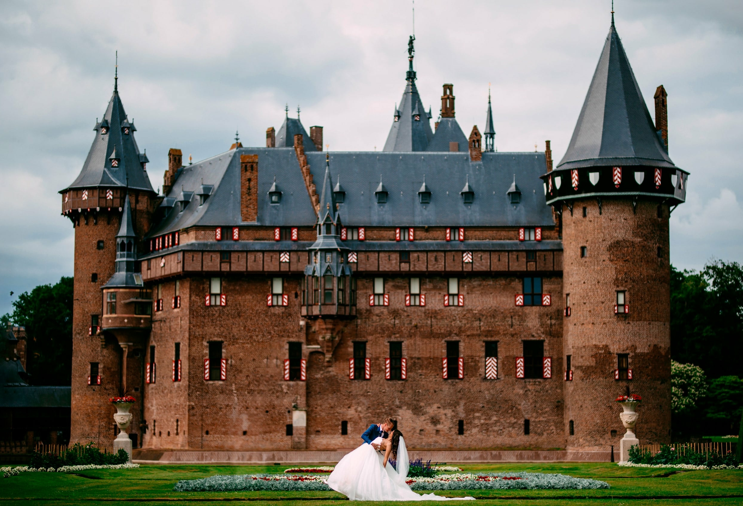 A bride and groom pose in front of a castle for their portfolio.