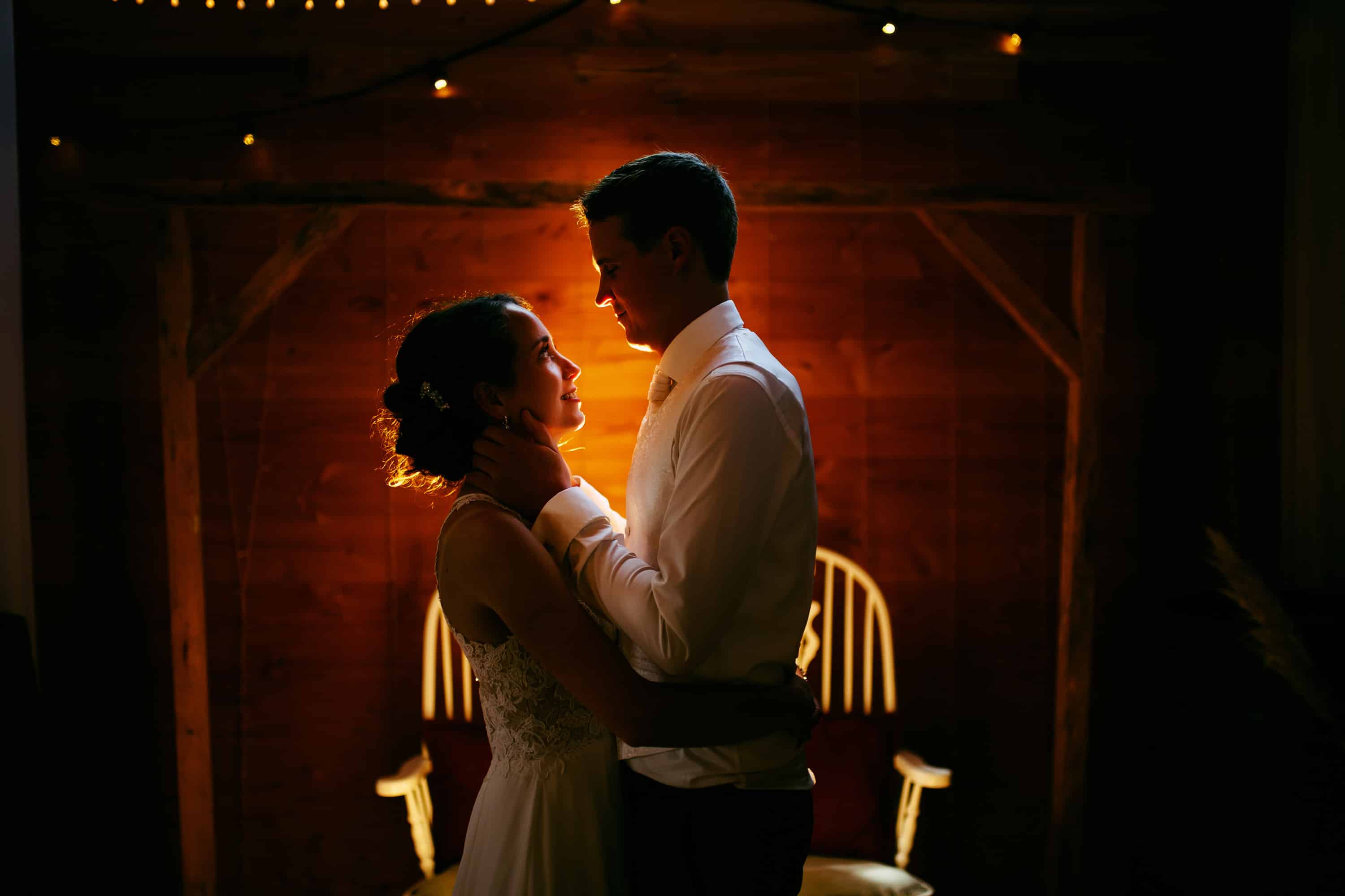 A bride and groom embrace in front of a wooden chair.