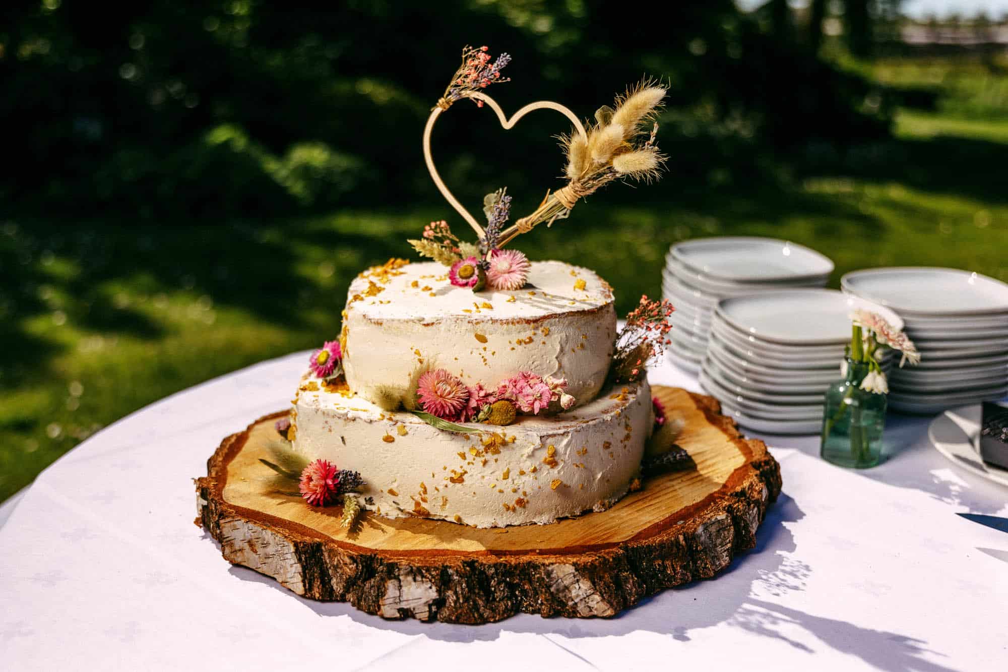 Beschrijving: Een bruidstaart met bloemen bovenop een houten plank.