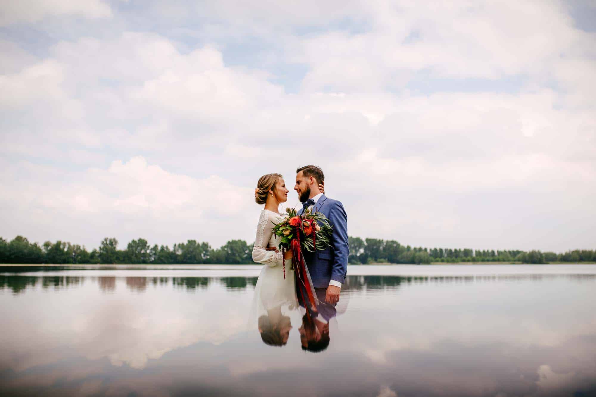 Bijzondere trouwfoto's van een bruid en bruidegom staande voor een meer.