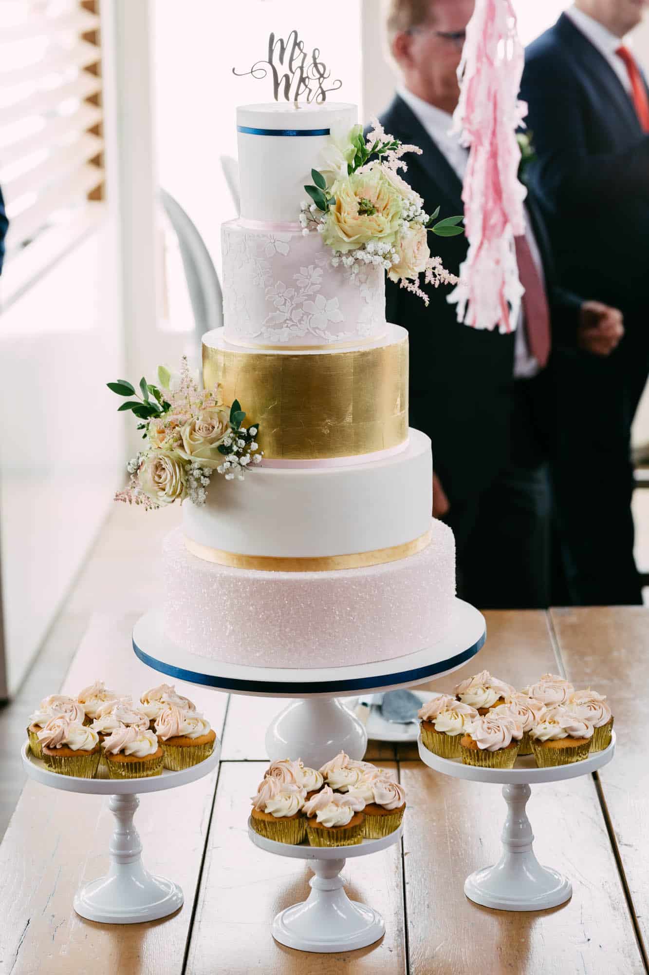 Wedding cakes sit on a table next to cupcakes.