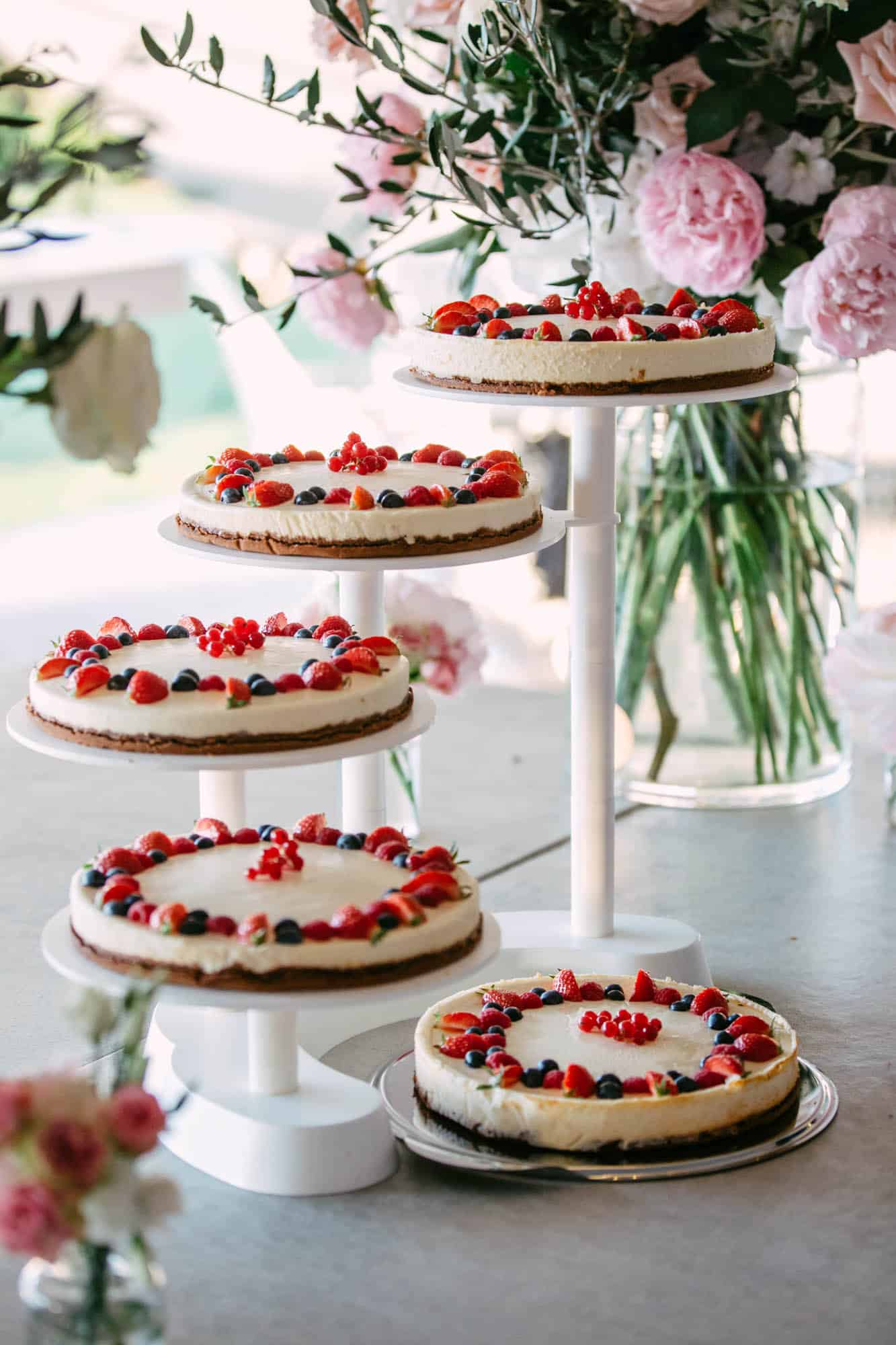 Three layers of cheesecakes on a table with beautiful wedding cake flowers.