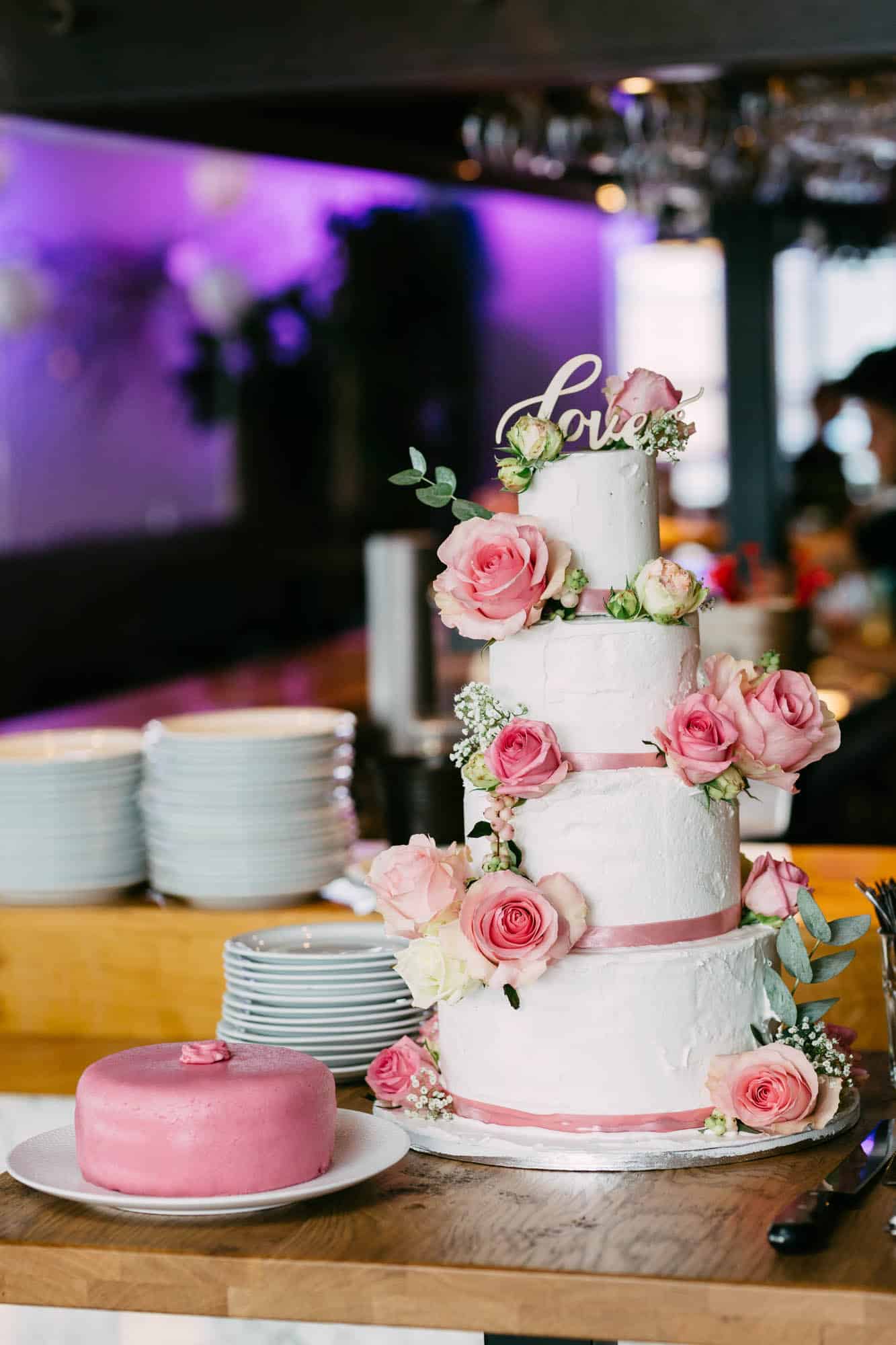White wedding cake with pink roses and love on top.