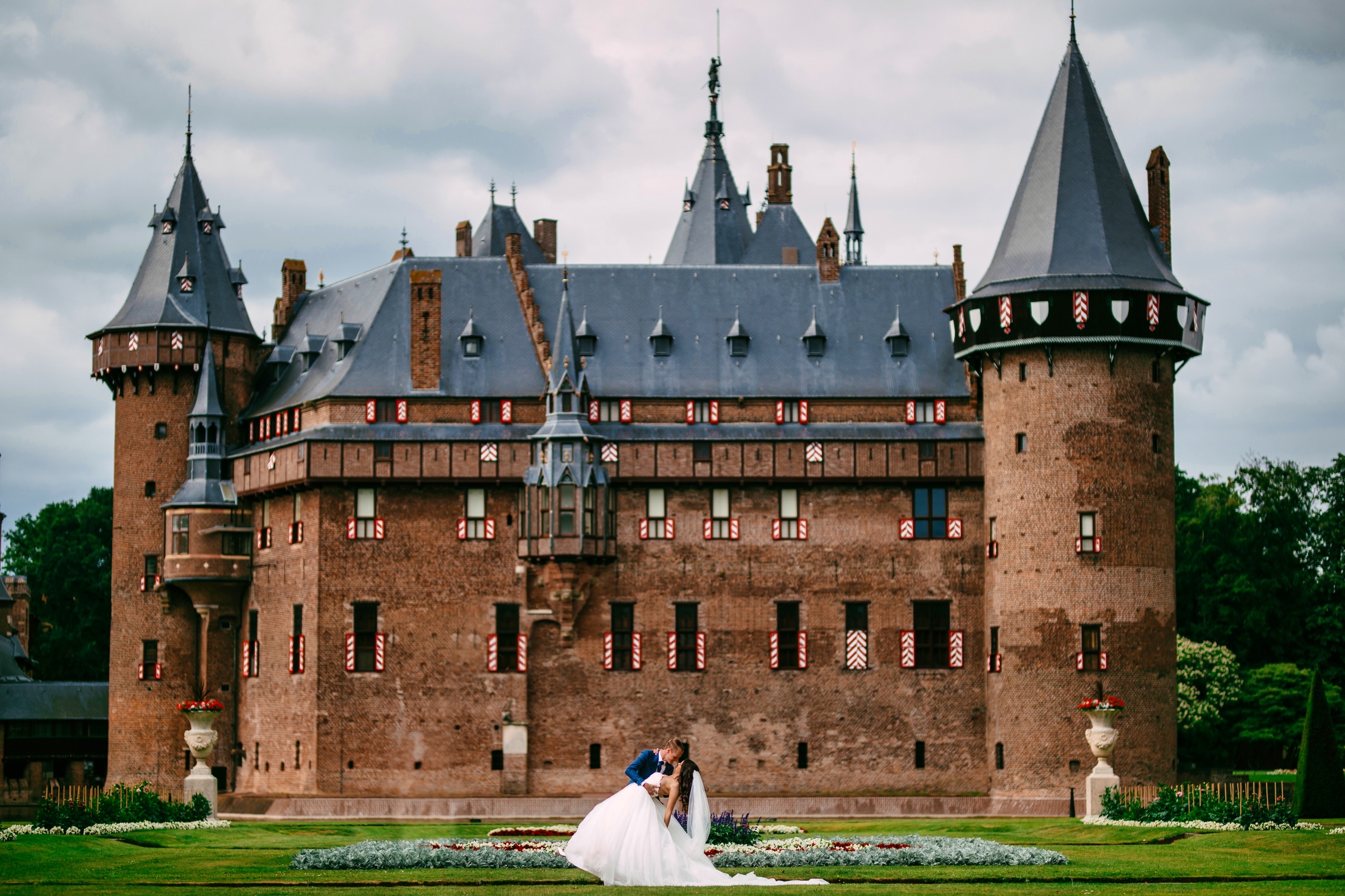 Een bruid en bruidegom poseren elegant voor een kasteel en laten de schoonheid van een A-lijn-trouwjurk zien.
